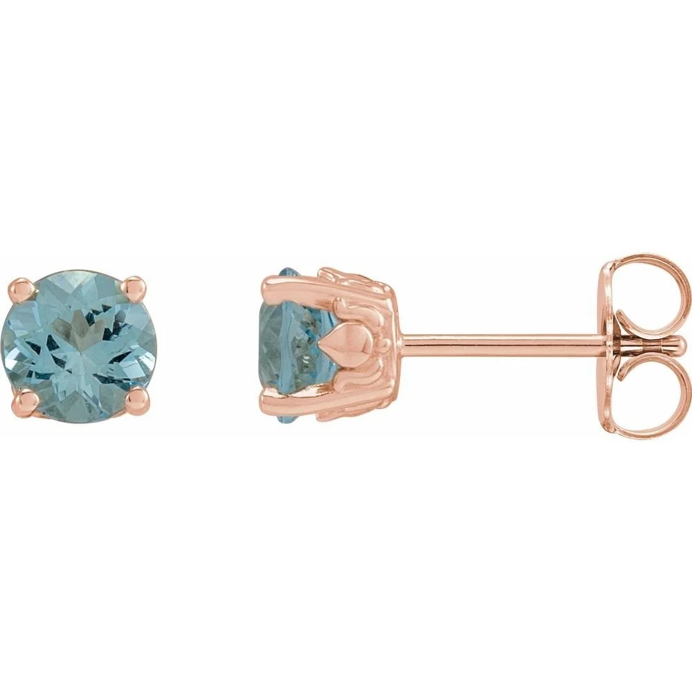 Close-up of a pair of stud earrings with round light blue gemstones set in rose gold prong settings.