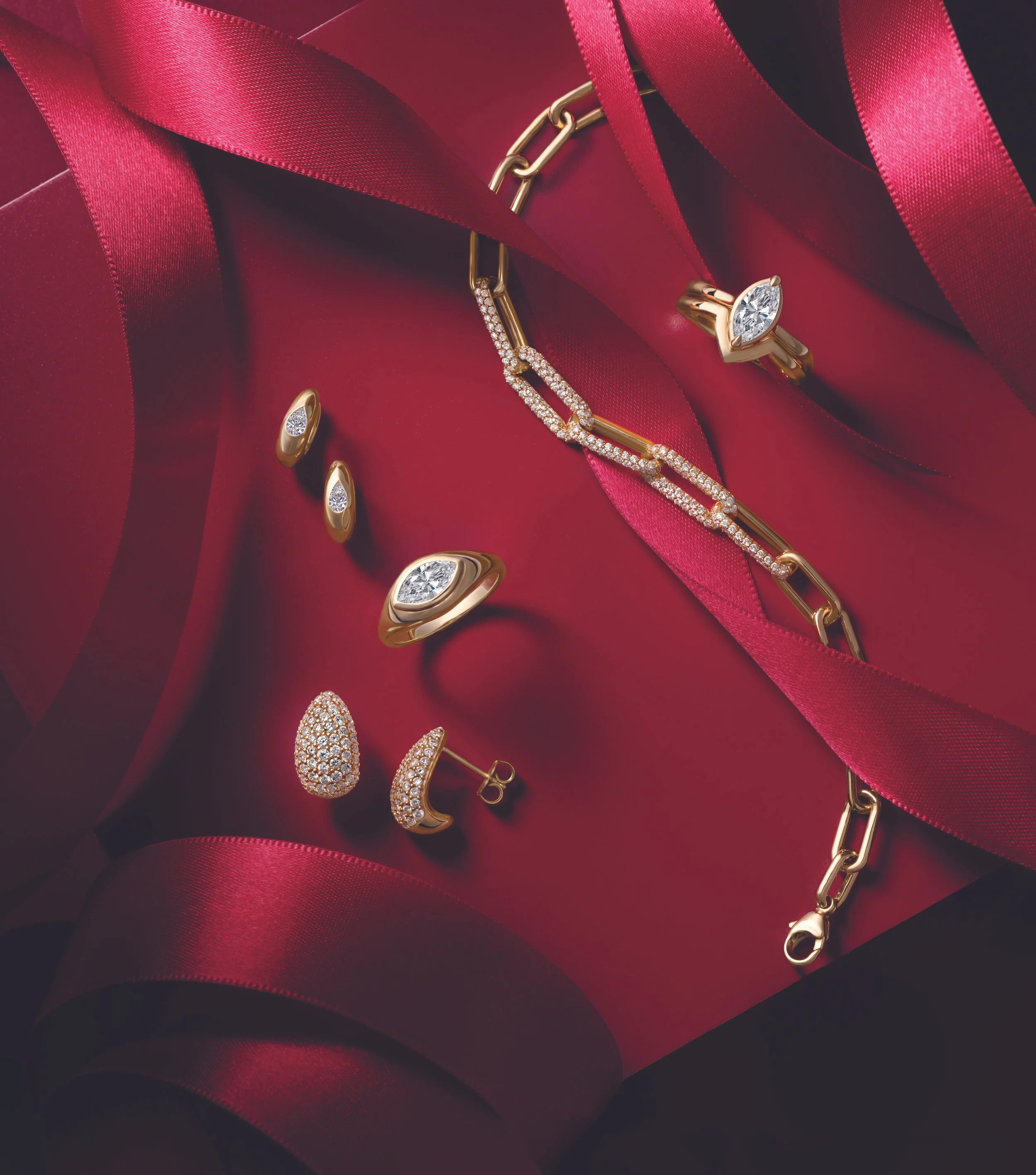 Elegant gold jewelry including a diamond ring, earrings, a bracelet, and a necklace, all adorned with diamonds, placed on red fabric with satin ribbons.