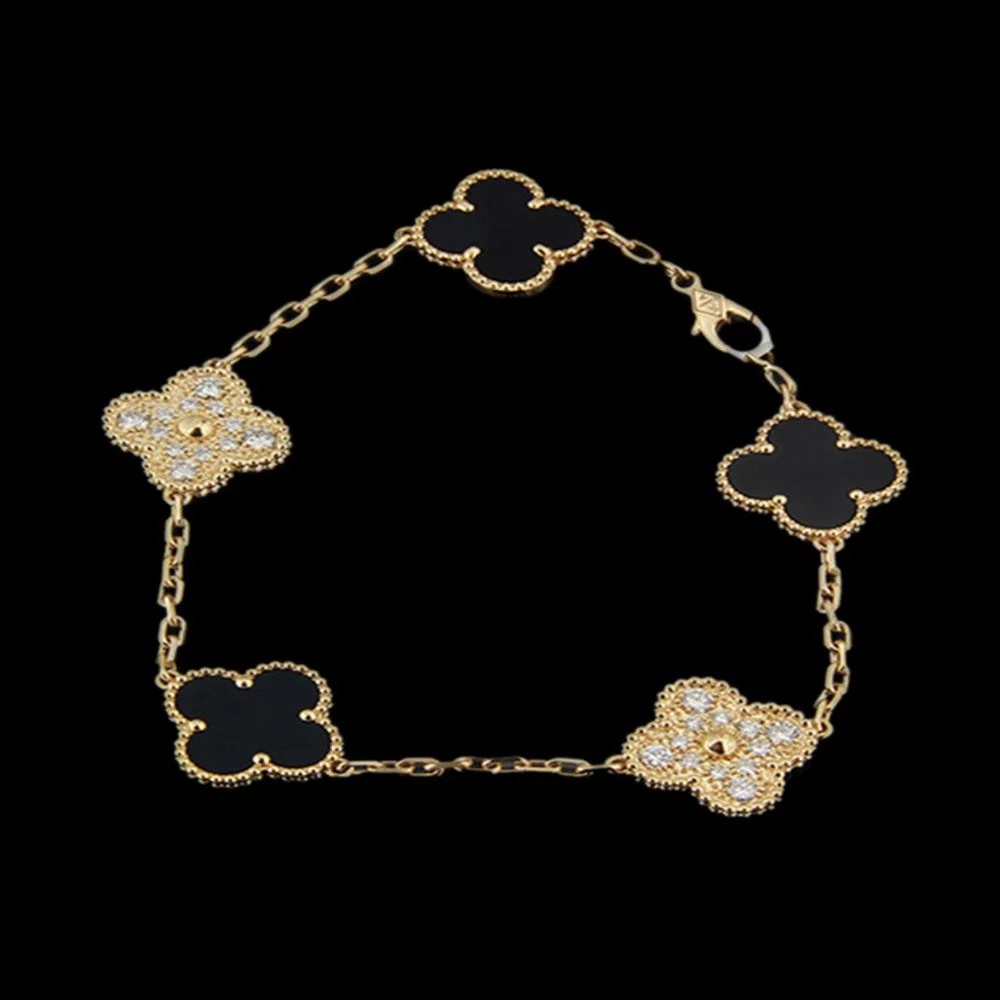Gold bracelet with four decorative clover-shaped charms, two with black inlays and two with white stones, on a black background.