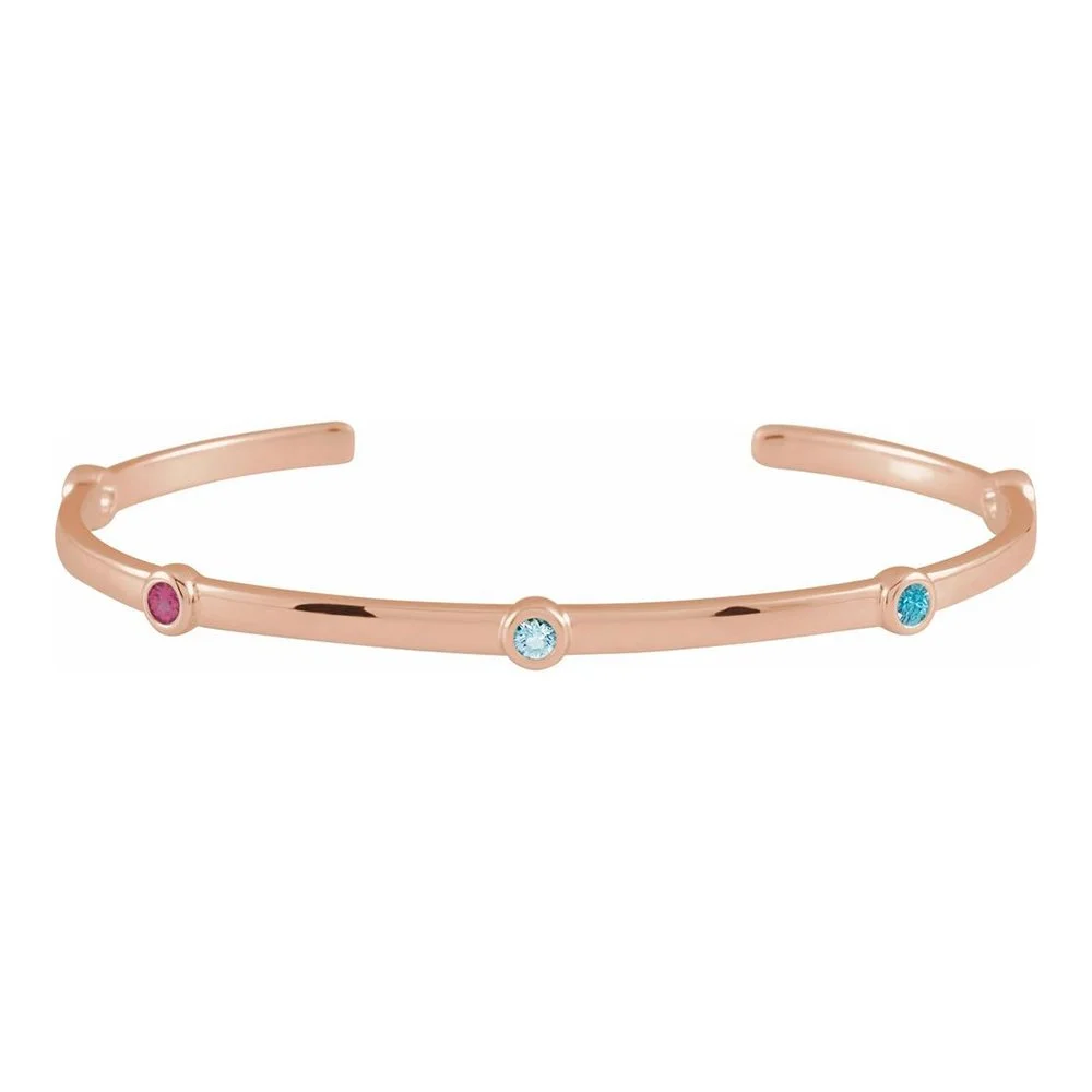 A rose gold open cuff bracelet with three evenly spaced round gemstones in pink, clear, and blue.