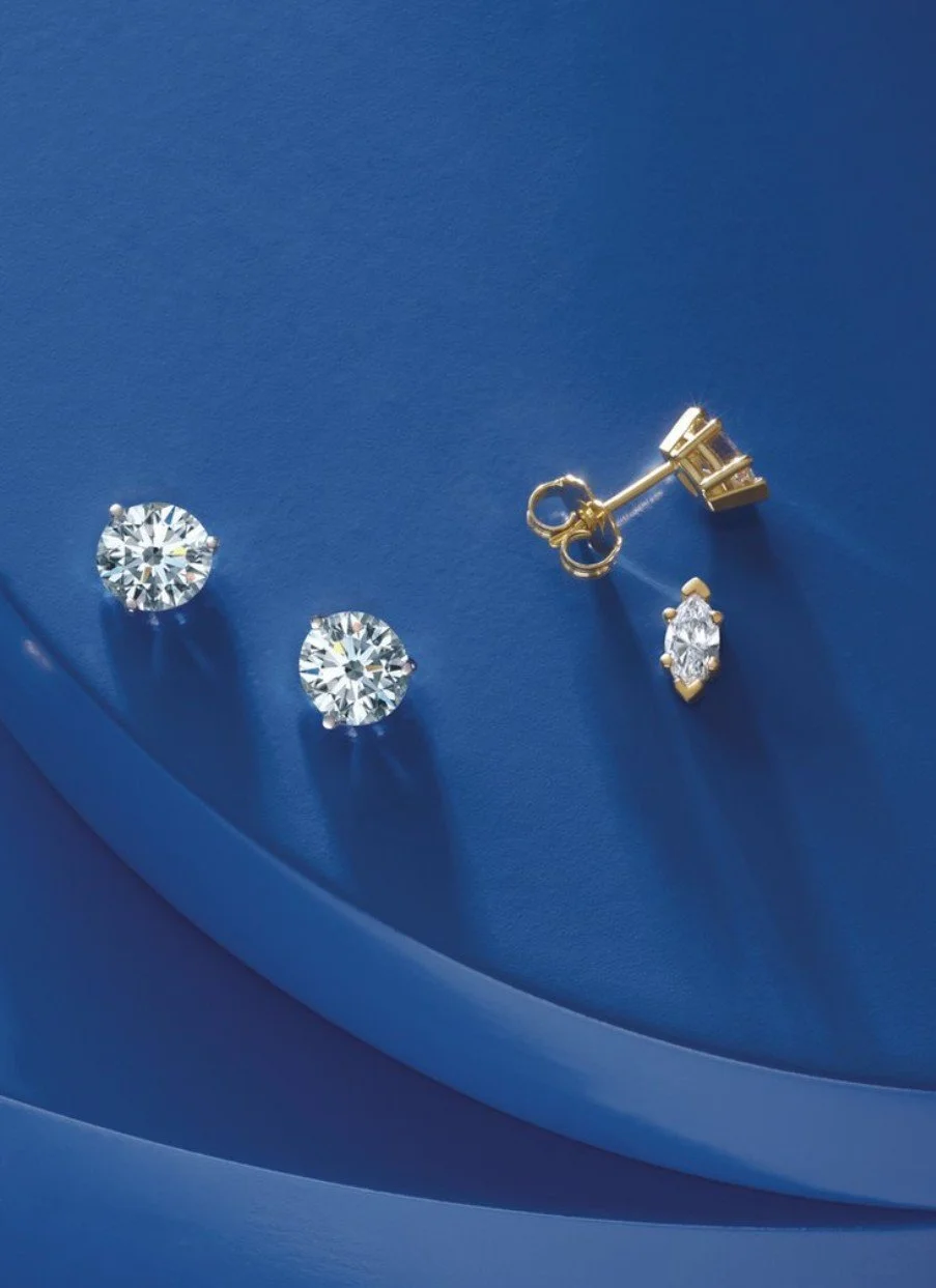 A pair of diamond stud earrings and a single diamond drop earring on a blue background.