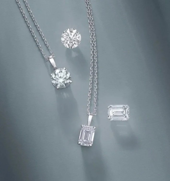 Two diamond necklaces, one with a round diamond pendant and the other with an emerald-cut diamond pendant, along with an emerald-cut diamond ring and a loose emerald-cut diamond gemstone