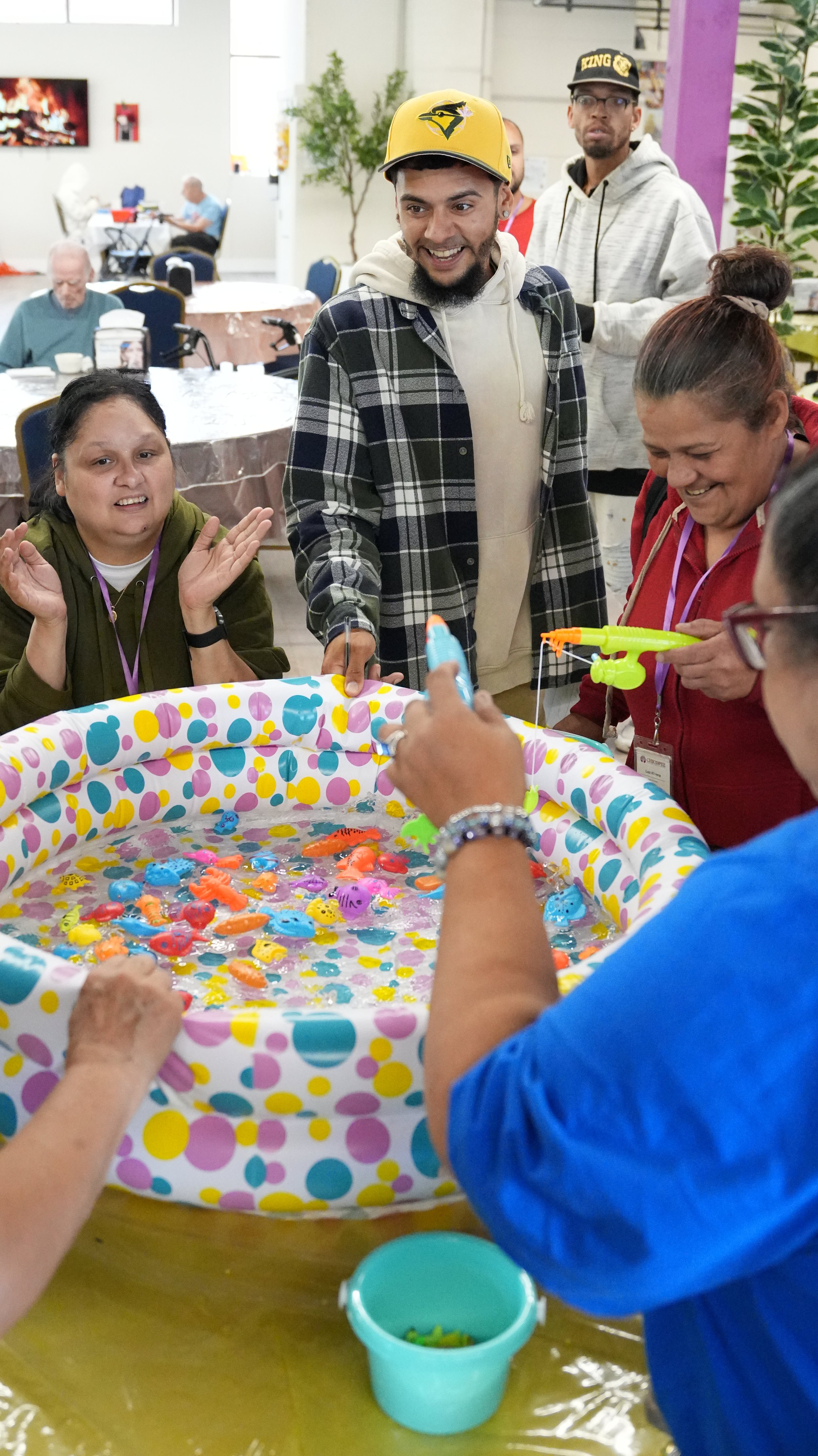People gathered around a small inflatable fish pond playing a fishing game with toy fish and small fishing poles.