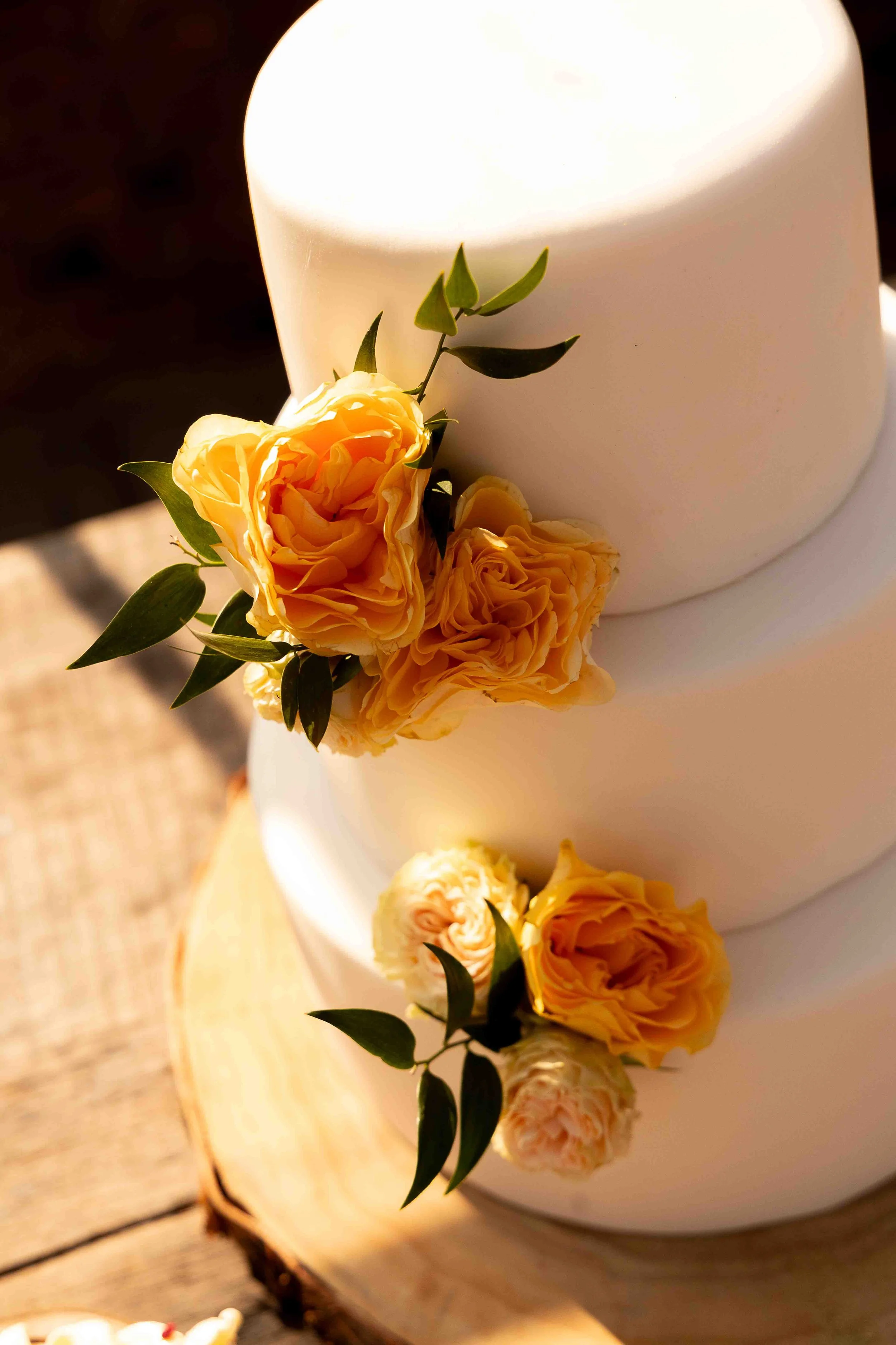 Een wit taart met gele bloemen en groene bladeren als decoratie.