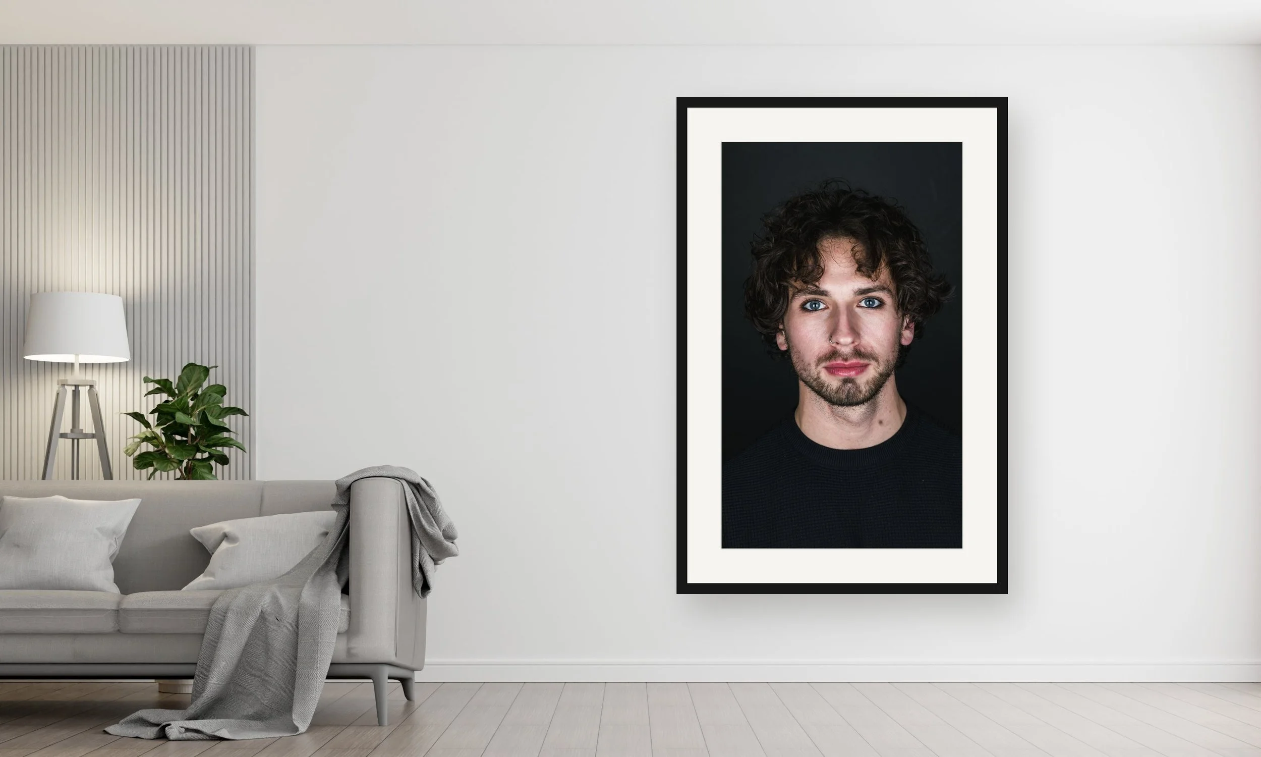 Een zwart-wit portretfoto van een jonge man met krullend haar en blauwe ogen, ingelijst aan de muur in een modern interieur.