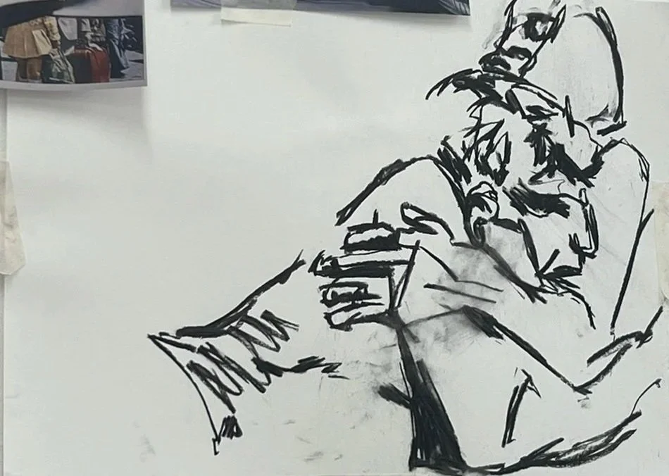 Line drawing of two people sitting, one reading a book, on a white wall with photographs in the background.