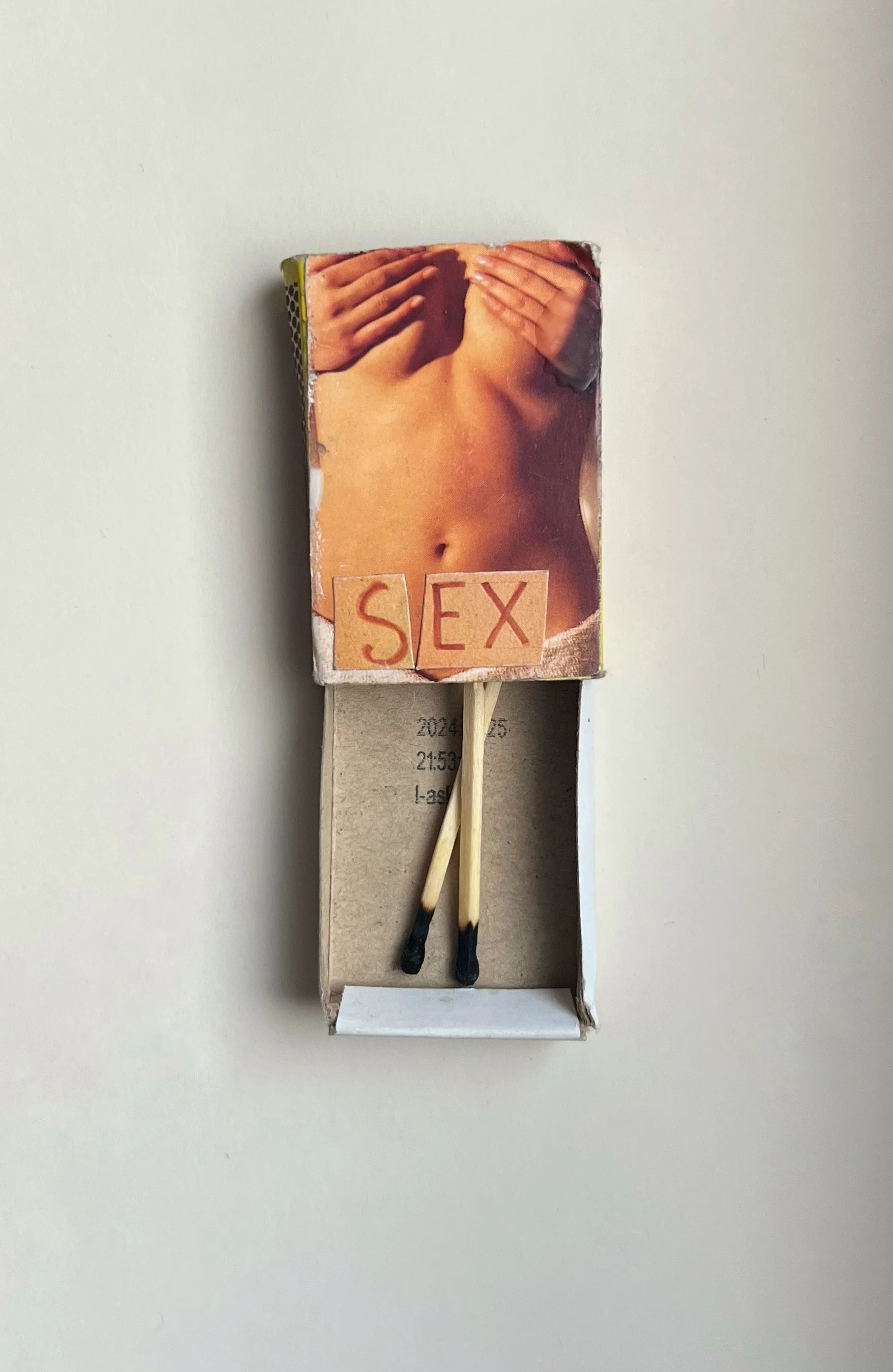 A matchstick pack with an image of a woman's bare torso and the word 'SEX' written on it, placed on a white surface.