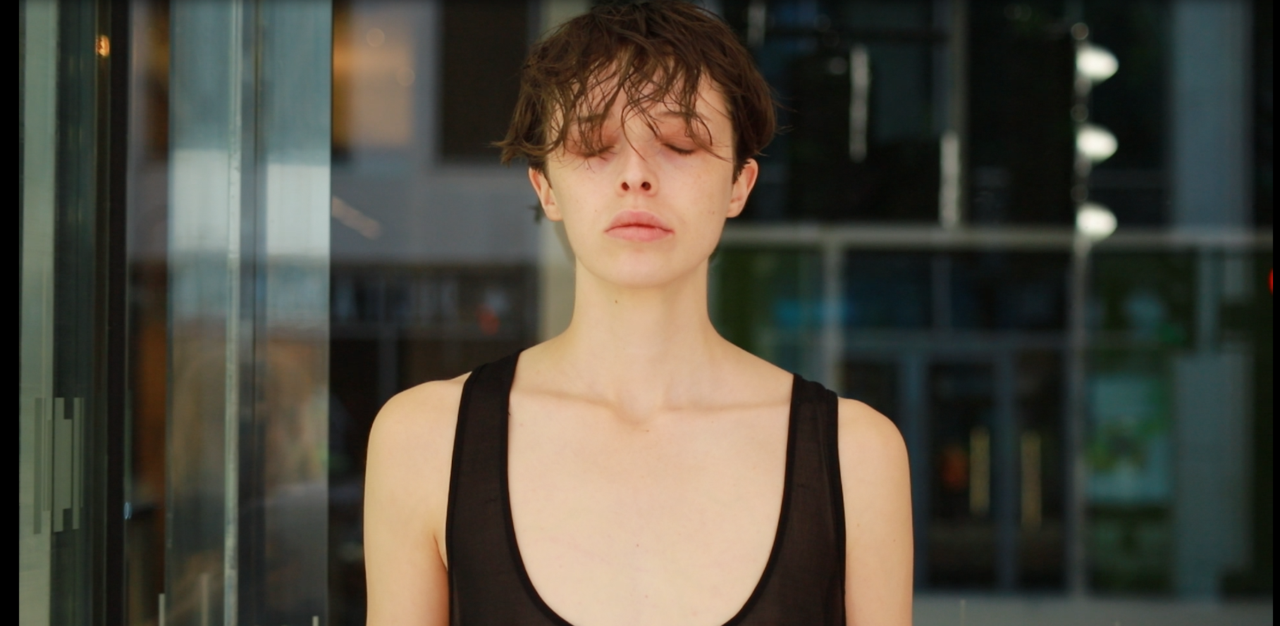 A young woman with short curly brown hair and fair skin standing outside with her eyes closed.