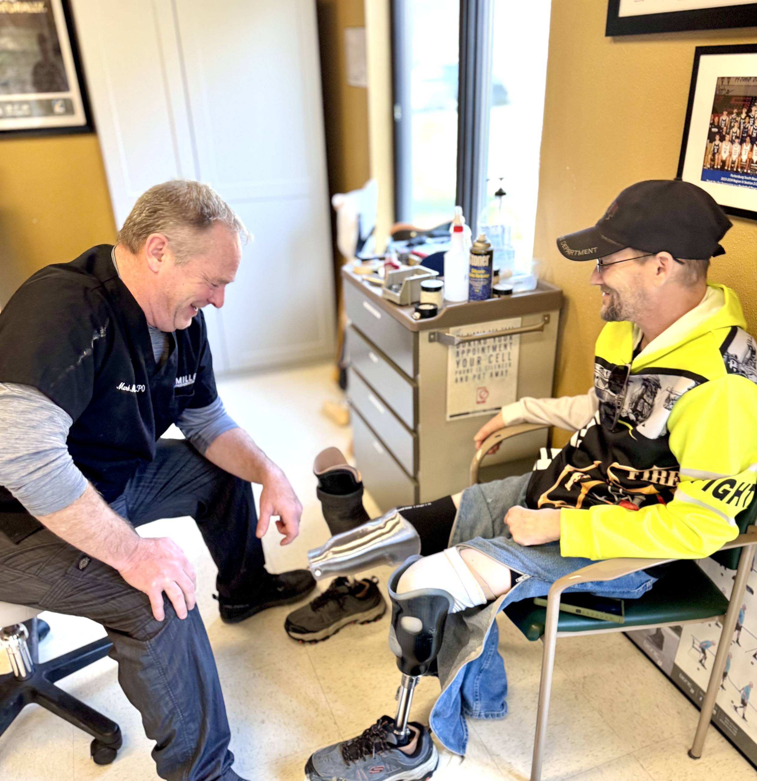 A doctor examining a man with a prosthetic leg in a medical office, both smiling.