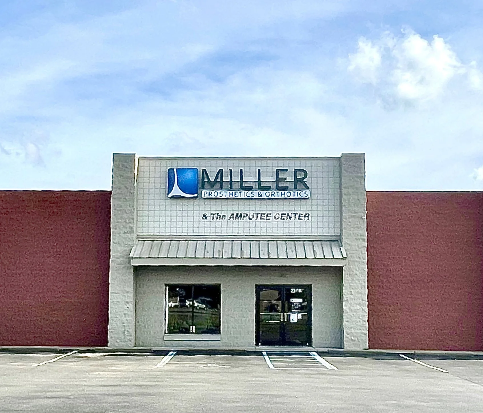 A storefront with a sign that reads "MLE R PROSTHETICS & ORTHOTICS & The AMPUTEE CENTER" showing a mostly empty parking lot and a blue sky with some clouds.