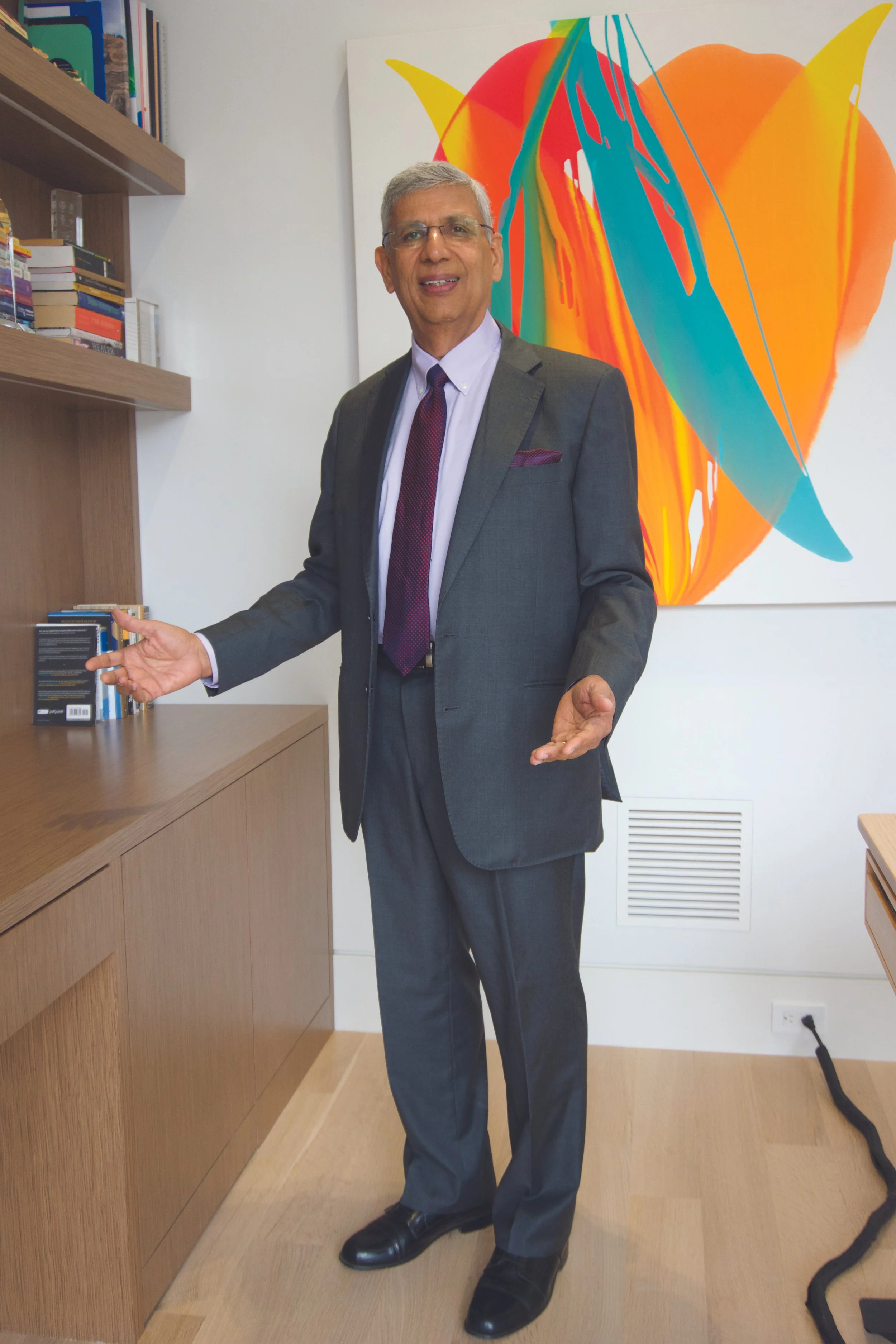 A man in a suit standing in a modern office with a colorful abstract art piece of a heart on the wall behind him.