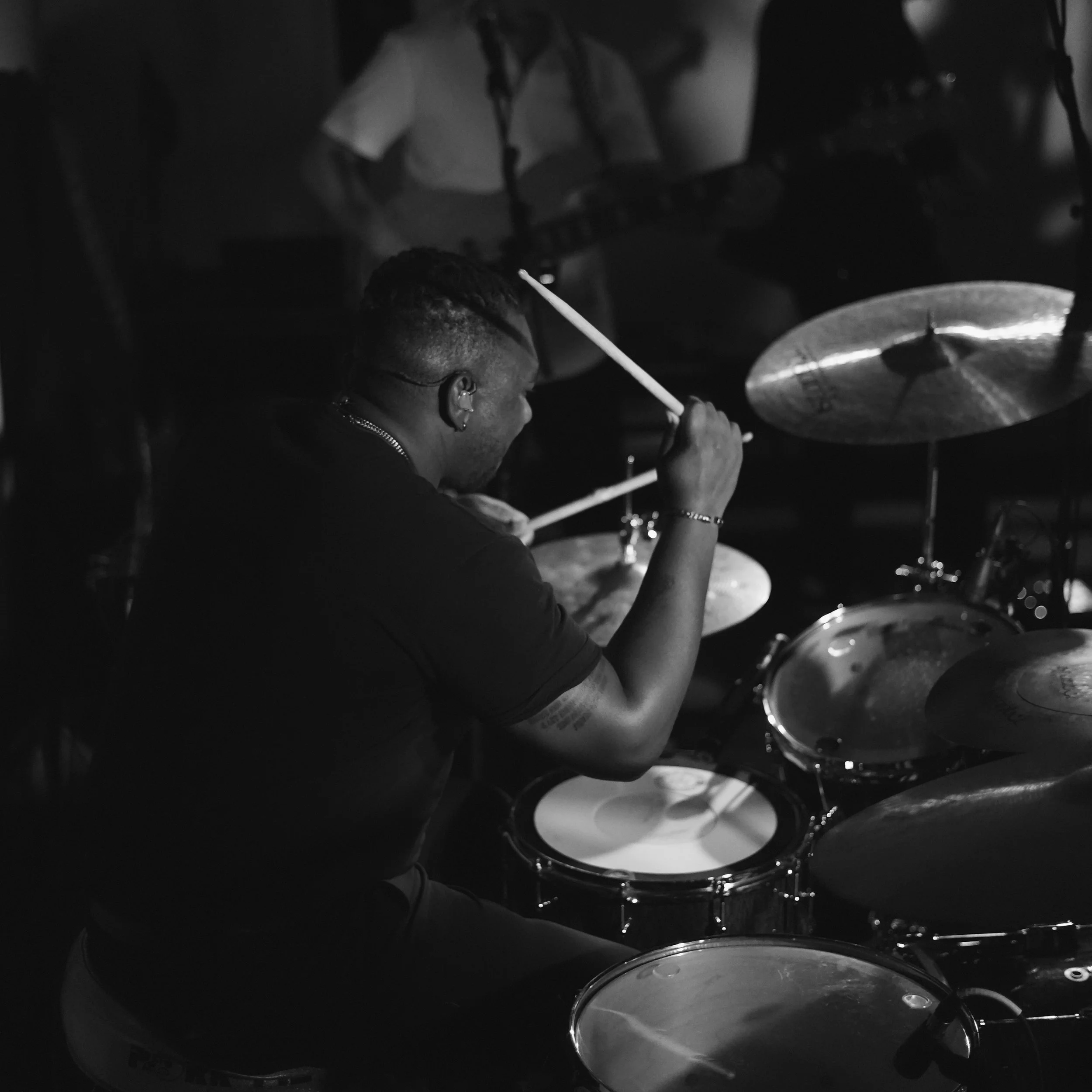 A person playing drums in a dark room, captured in black and white.