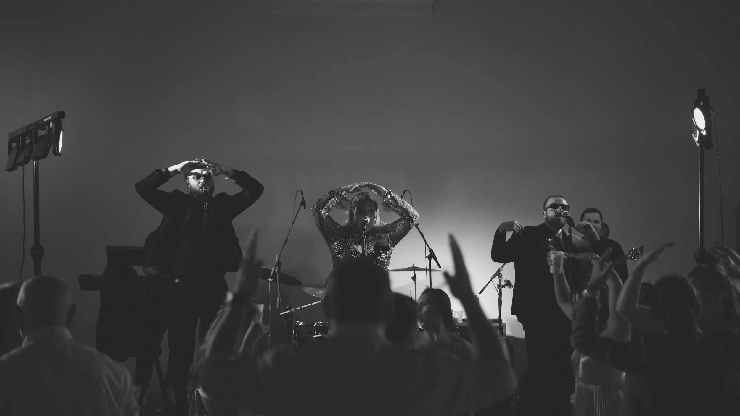 A black and white photo of a band performing live on stage with audience members dancing and raising their hands.