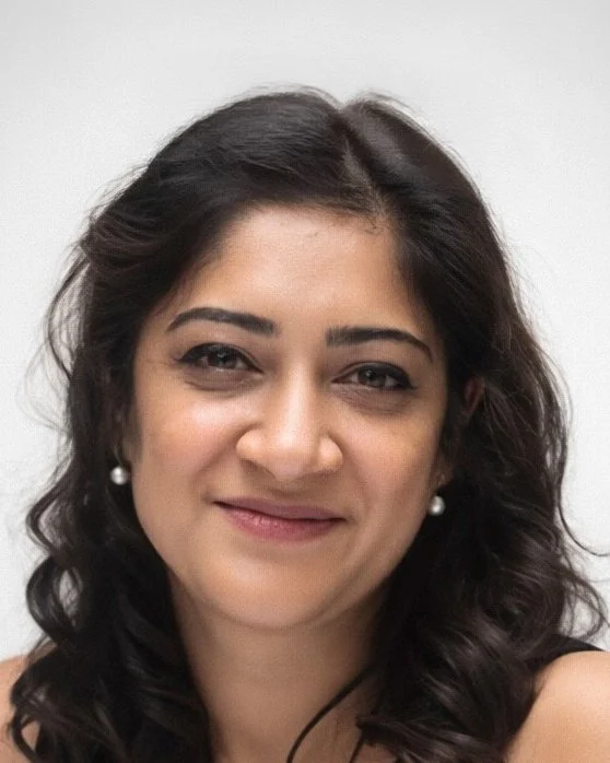 Close-up of a woman with dark wavy hair, pearl earrings, and a slight smile, against a white background.