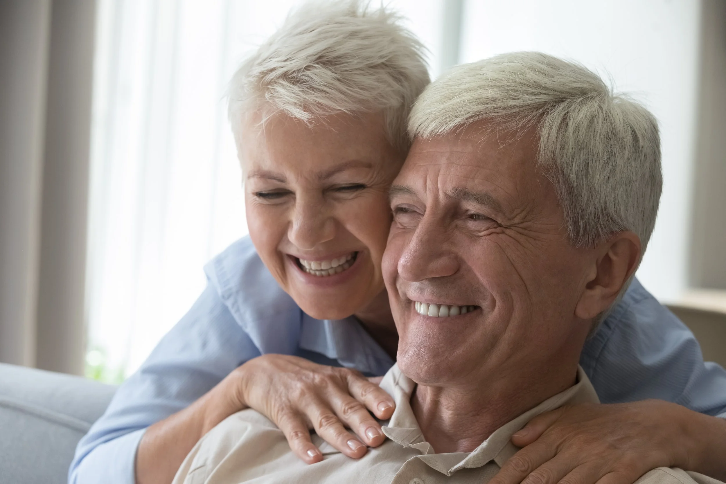 Elderly couple laughing and hugging each other indoors.