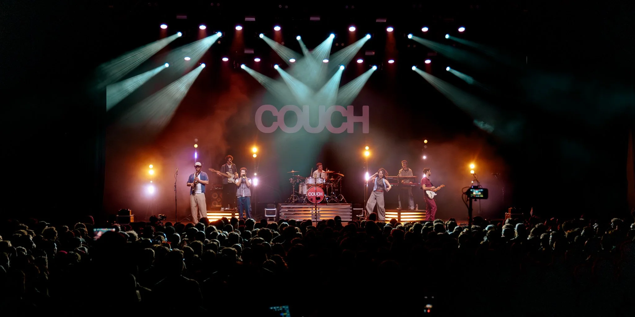 A live music concert on stage with a band called 'Couch' performing under colorful stage lighting, with an audience watching.