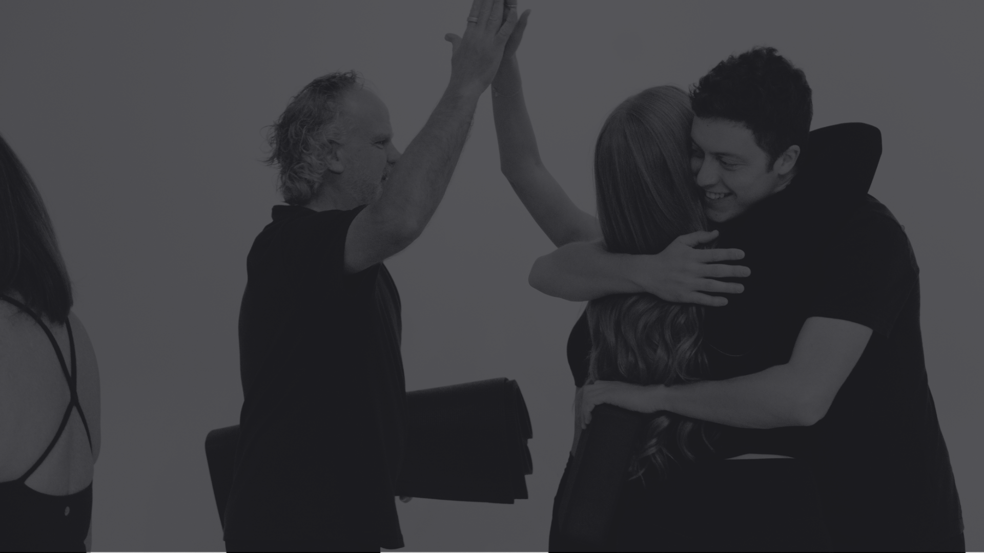 Two people hugging and smiling while another person is giving a high five in the background.