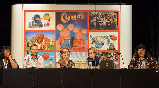 A panel of five people sitting at a table in front of a collage of images of Muppets and characters from Sesame Street, with a sign that reads 'Clangers' in the center.