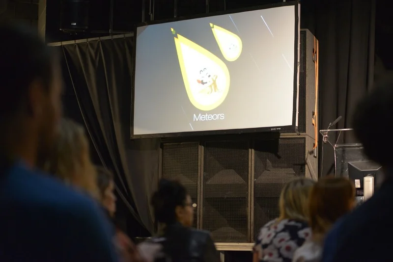 A presentation on meteors projected on a large screen in a dark room with an audience watching.
