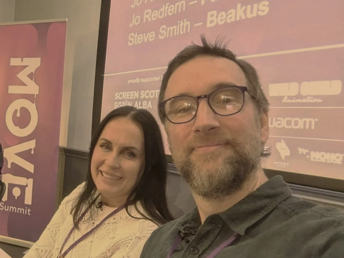 Beakus producer Steve Smith and Jo Redfern taking a selfie at the MOVE Summit, with a purple and pink conference banner and a large screen in the background.