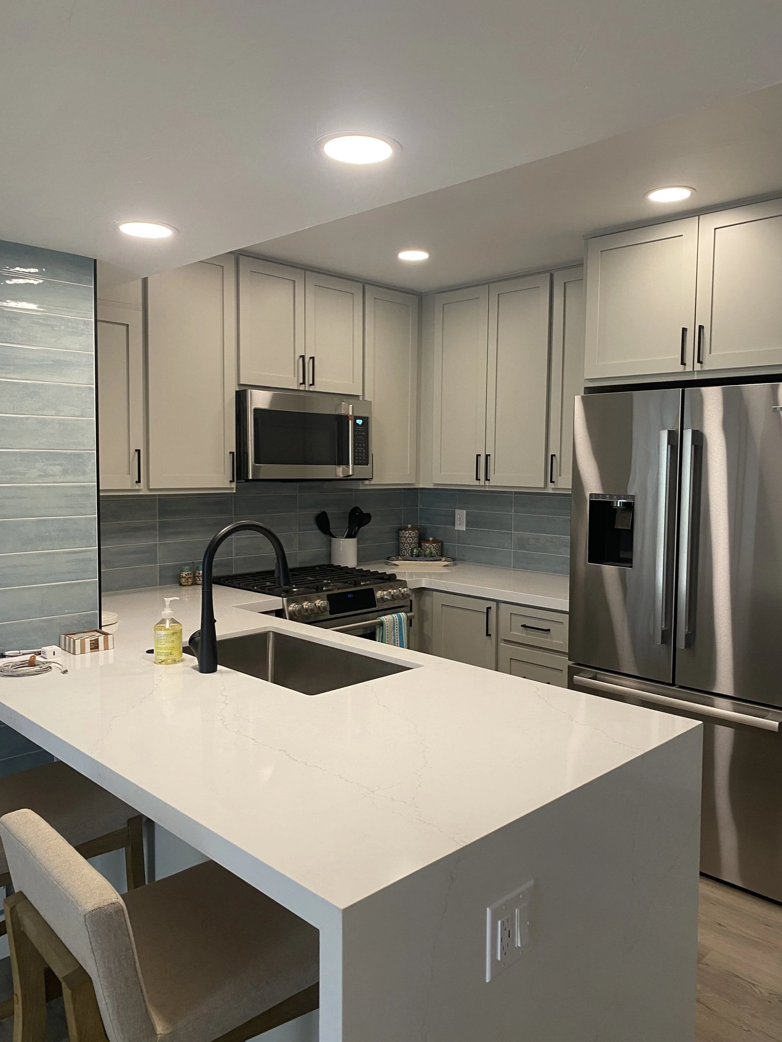Modern kitchen with white countertops, gray cabinets, stainless steel appliances, and a black faucet in the island.
