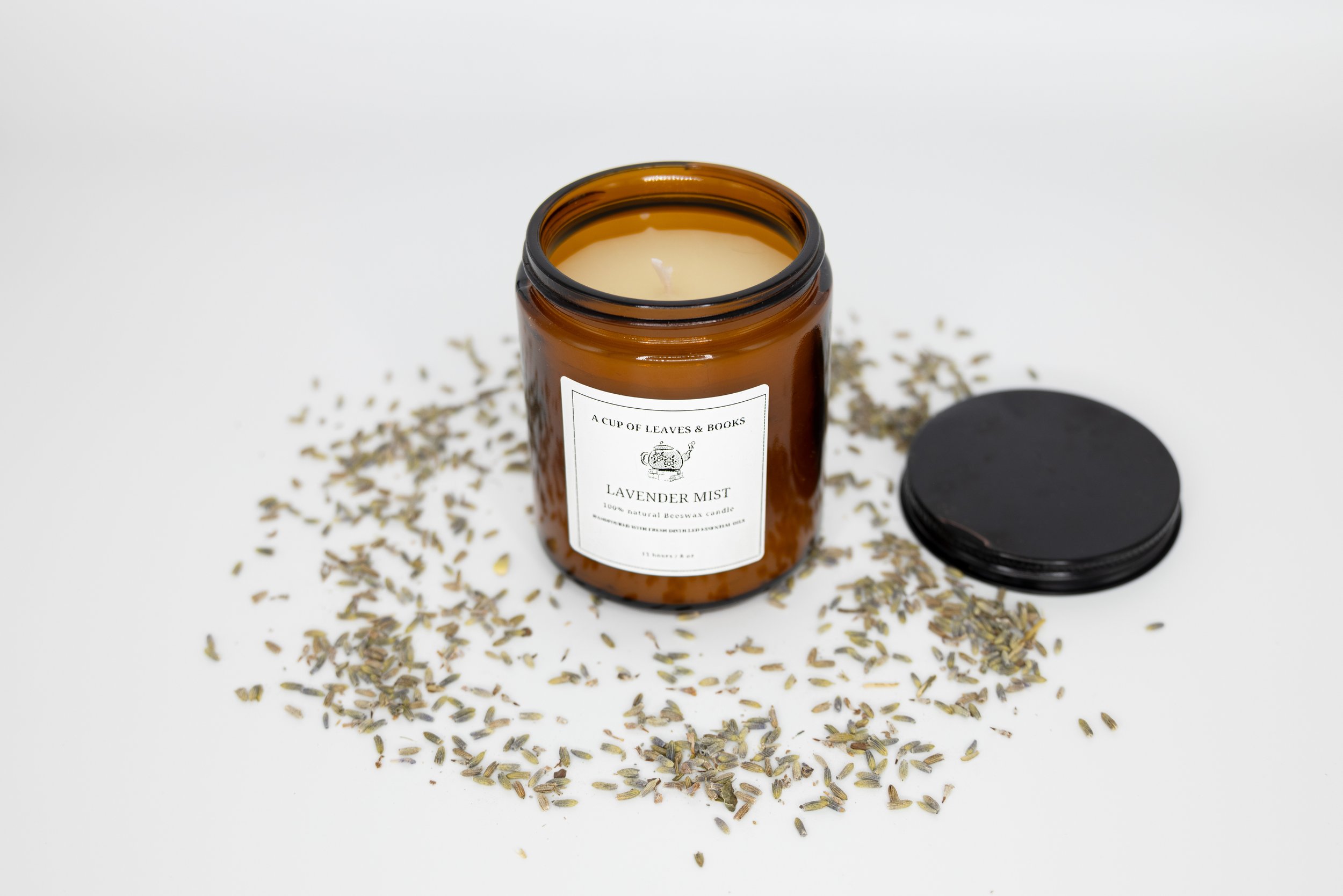 An amber glass jar labeled 'Lavender Mist' with a black lid off, surrounded by dried lavender flowers on a white background.