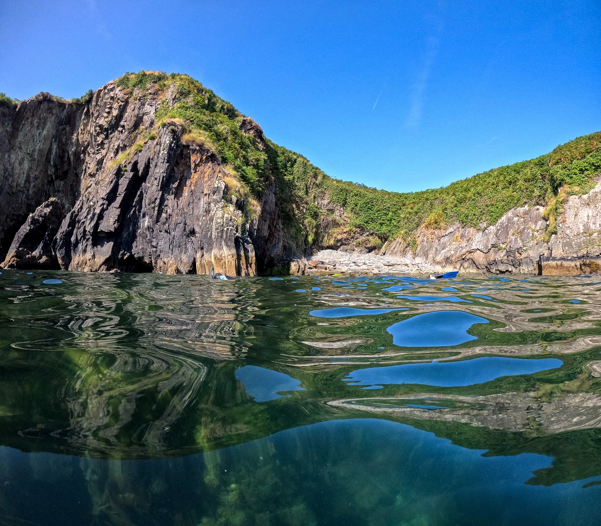 picture of green sea, in Cork, Ireland, beautiful cliff and scenery and a person snorkelling under blue sky