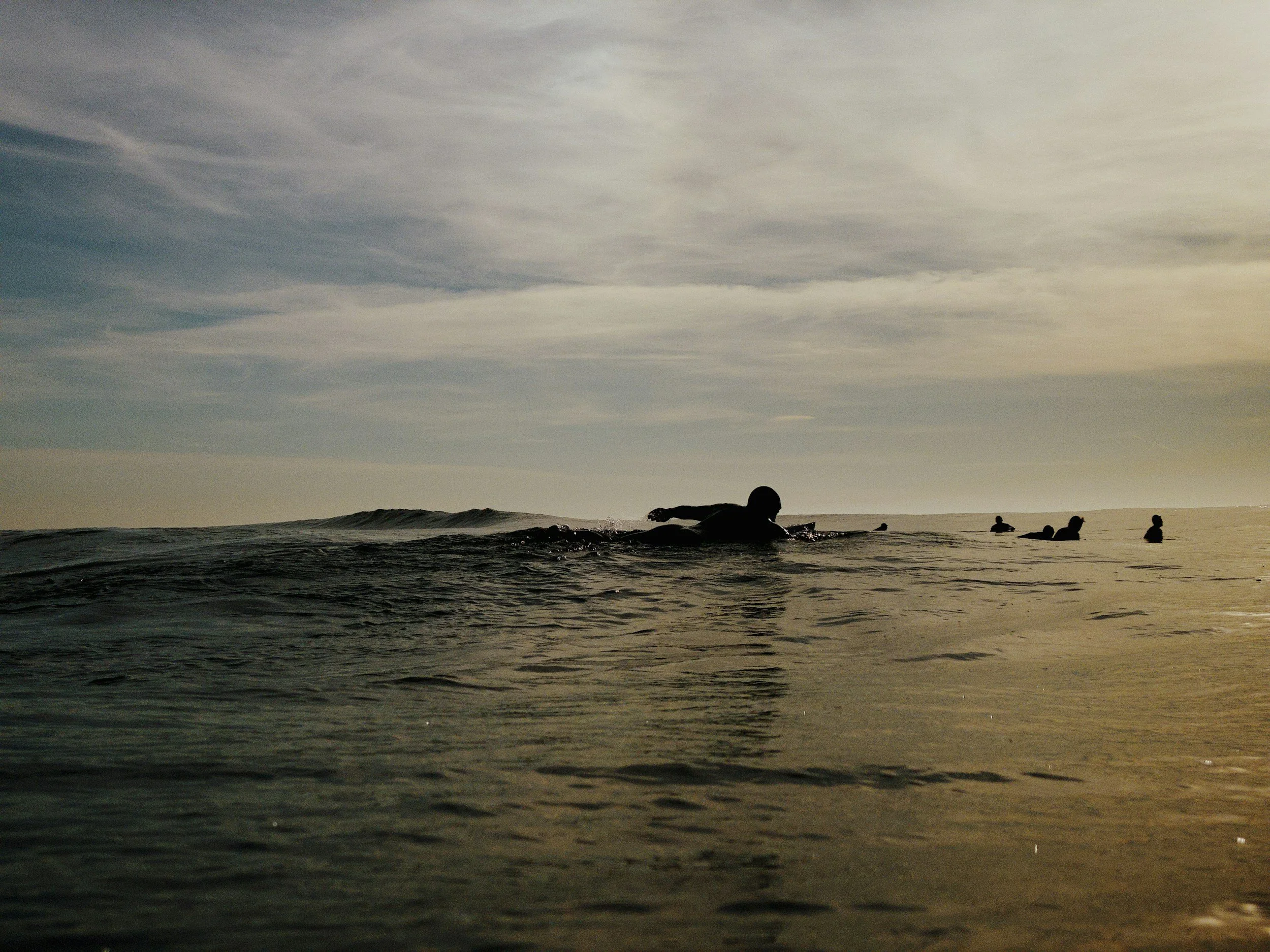 A person swimming in the ocean with several others in the background during sunset.