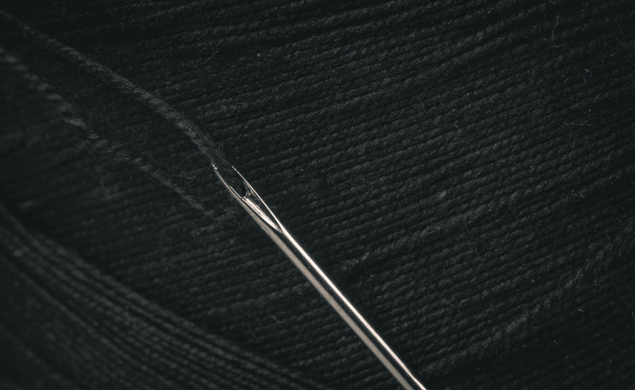 Close-up of sewing needle partially embedded in black fabric.