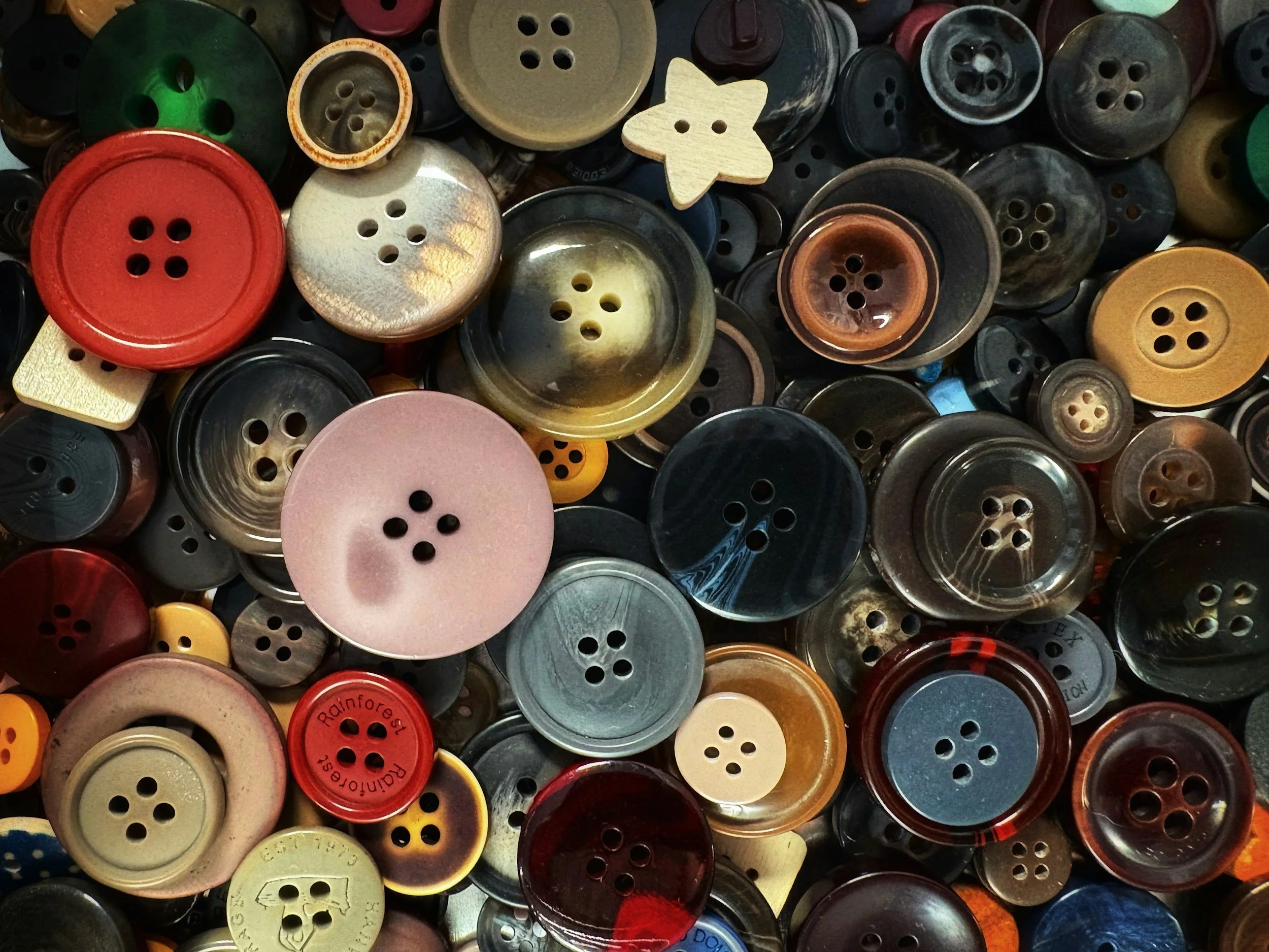 A collection of various colored buttons, some with four holes, others with two, in different sizes and materials like plastic and wood.