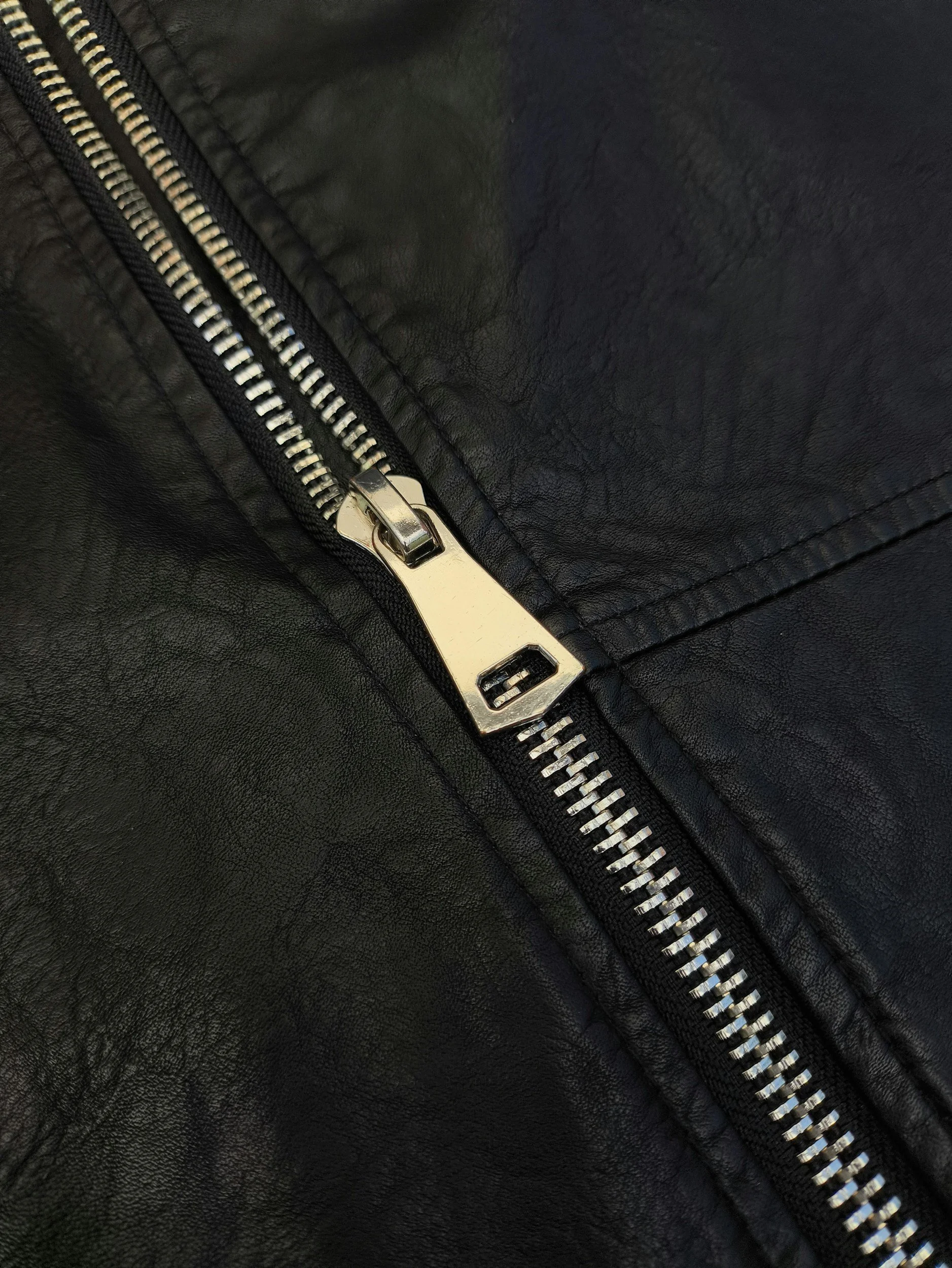 Close-up of a black leather jacket zipper with a silver pull tab.