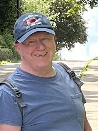 Smiling man in a blue t-shirt and baseball cap outdoors.