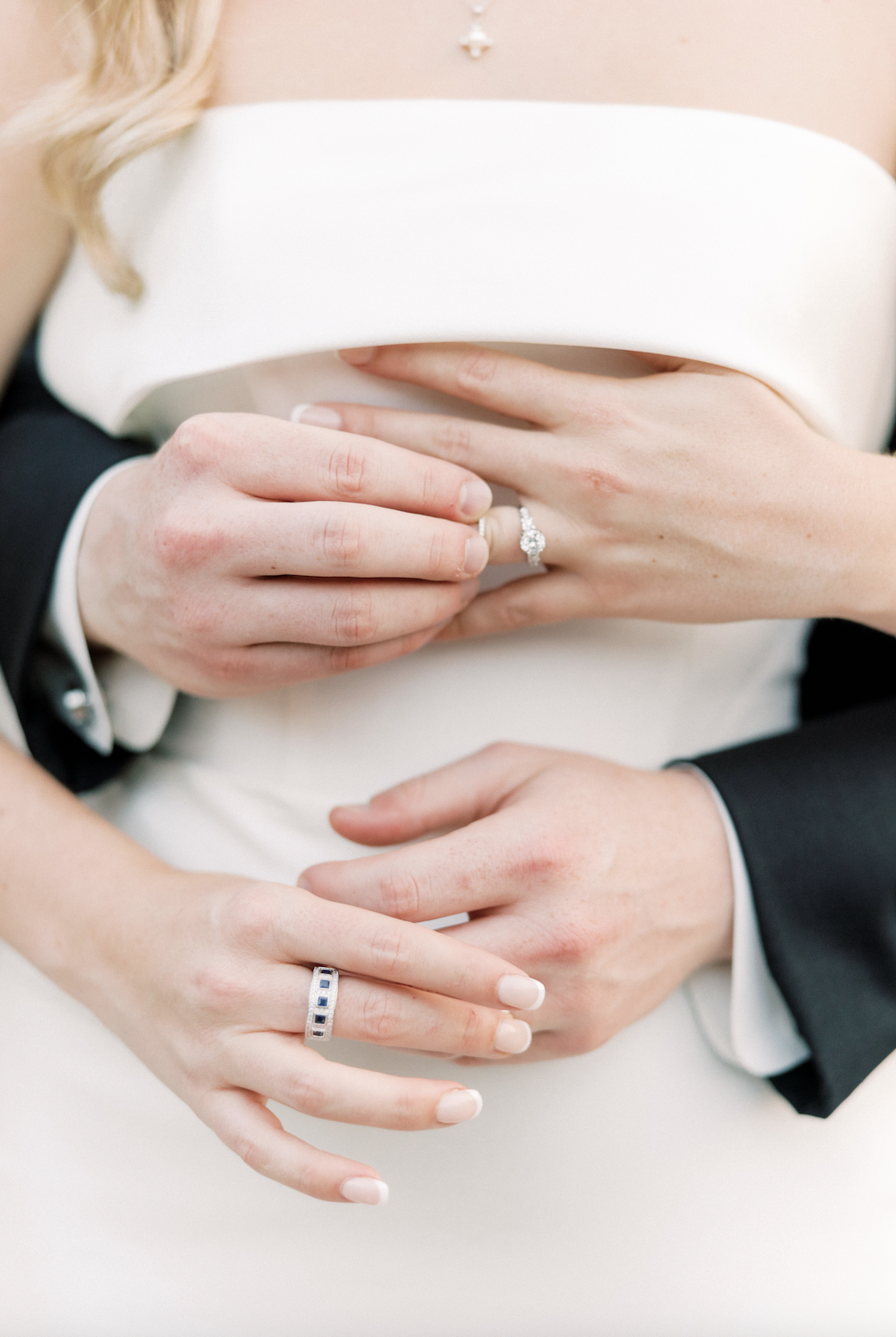 Close-up of a bride and groom's hands showing wedding rings, with a focus on the bride's rings and jewelry.