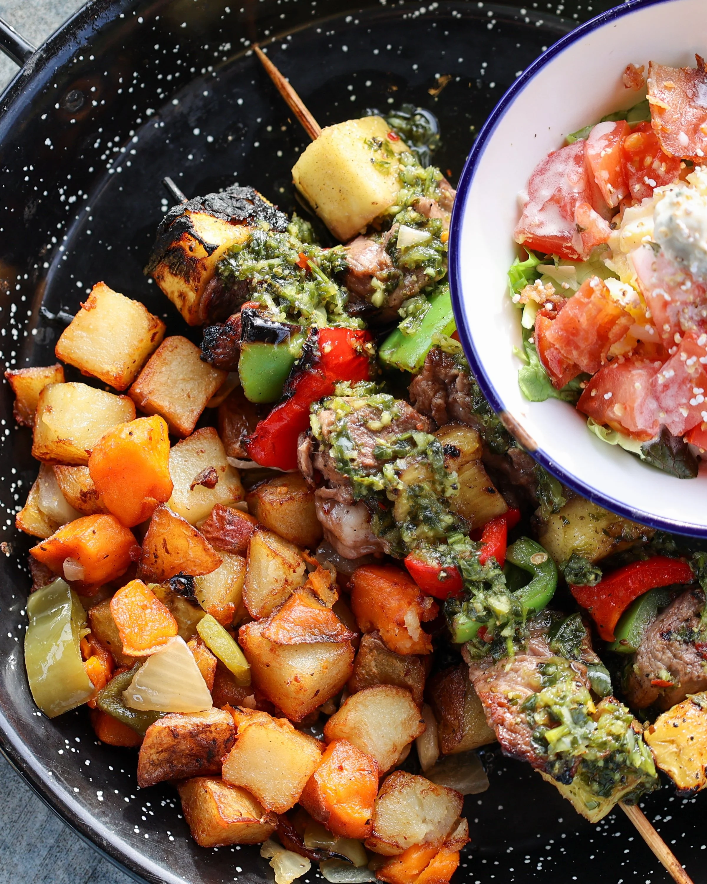 Cooked roasted vegetables, including potatoes, carrots, bell peppers, and zucchini, served with a side salad of chopped lettuce, tomatoes, and crumbled cheese.