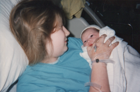 A woman lying in a hospital bed holding a newborn baby wrapped in a white blanket.