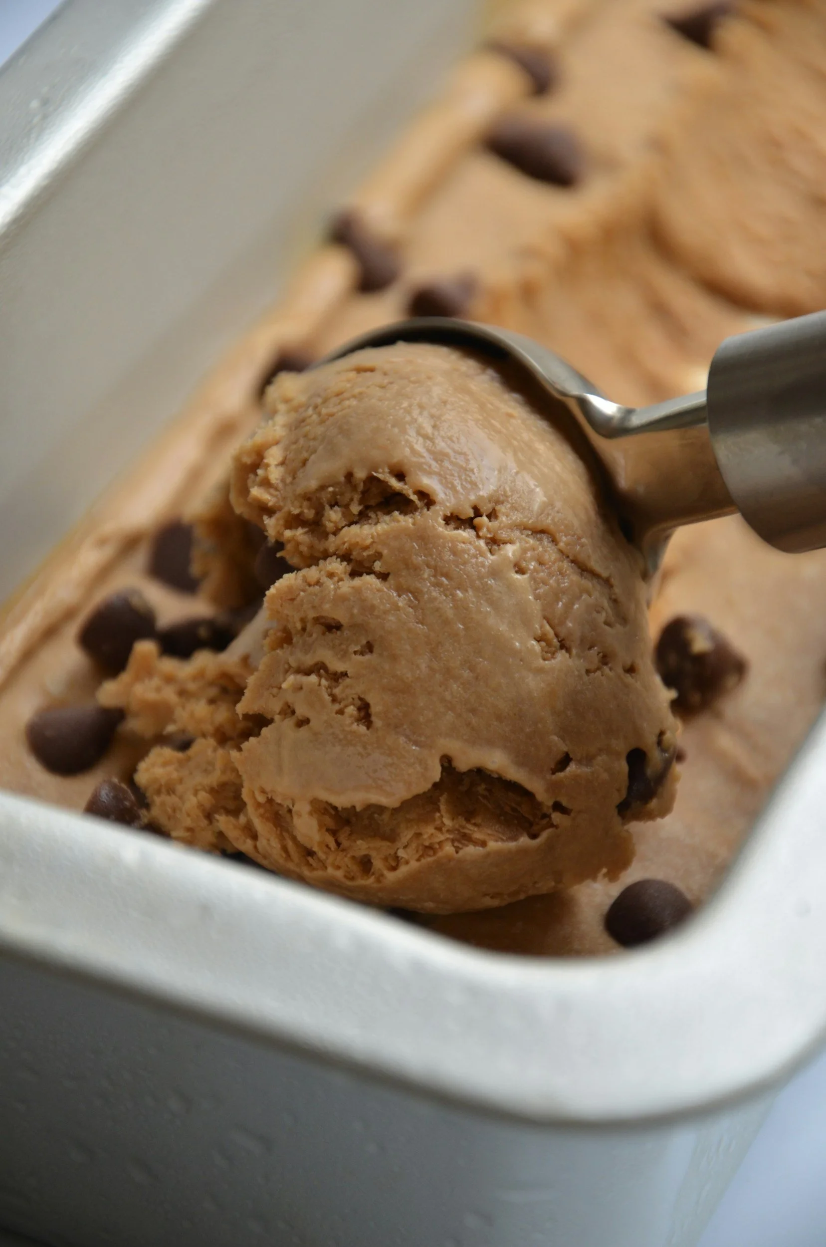 Close-up of a container with a scoop of chocolate chip cookie dough, with chocolate chips visible, ready to be frozen or baked.