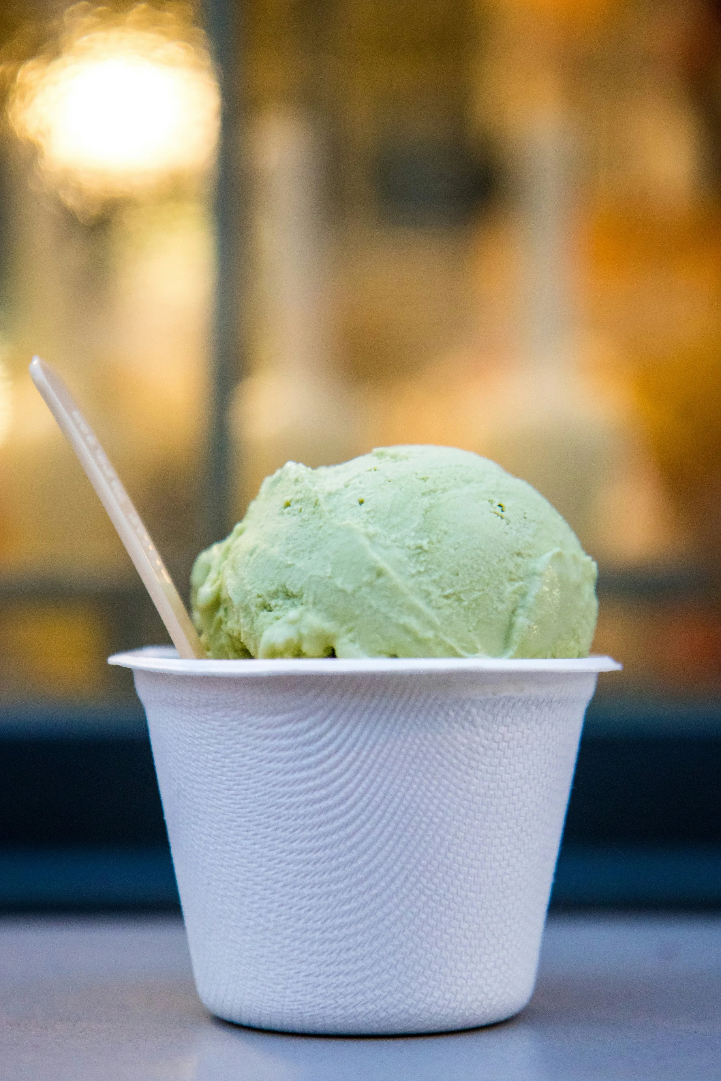A single scoop of green ice cream in a white paper cup with a small plastic spoon.