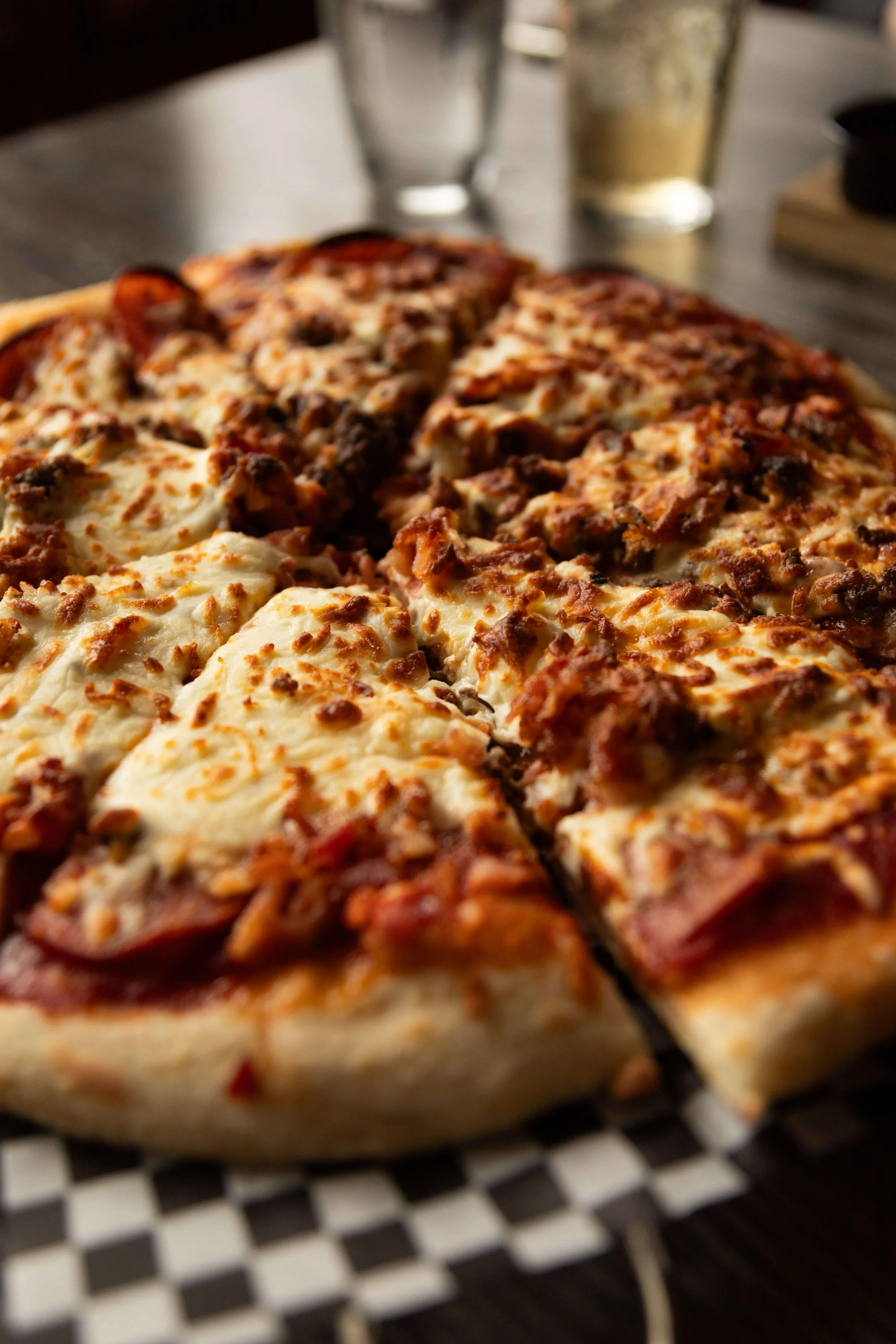 Close-up of a slice of pizza with cheese, sausage, and beef toppings on a plate with a black and white checkered pattern.