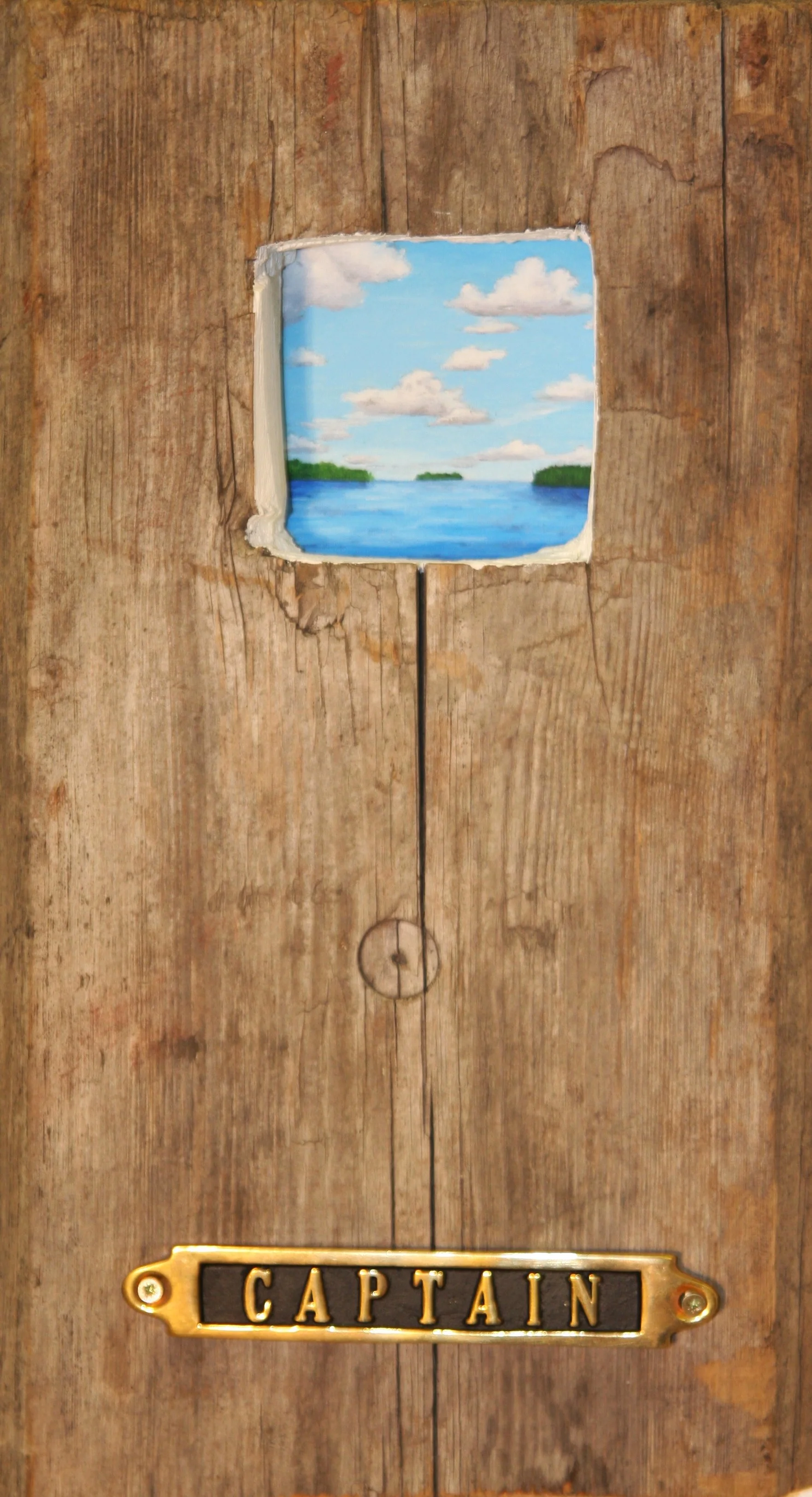 A wooden door with a small painted window showing a lake and sky with clouds, and a brass nameplate labeled 'CAPTAIN'.