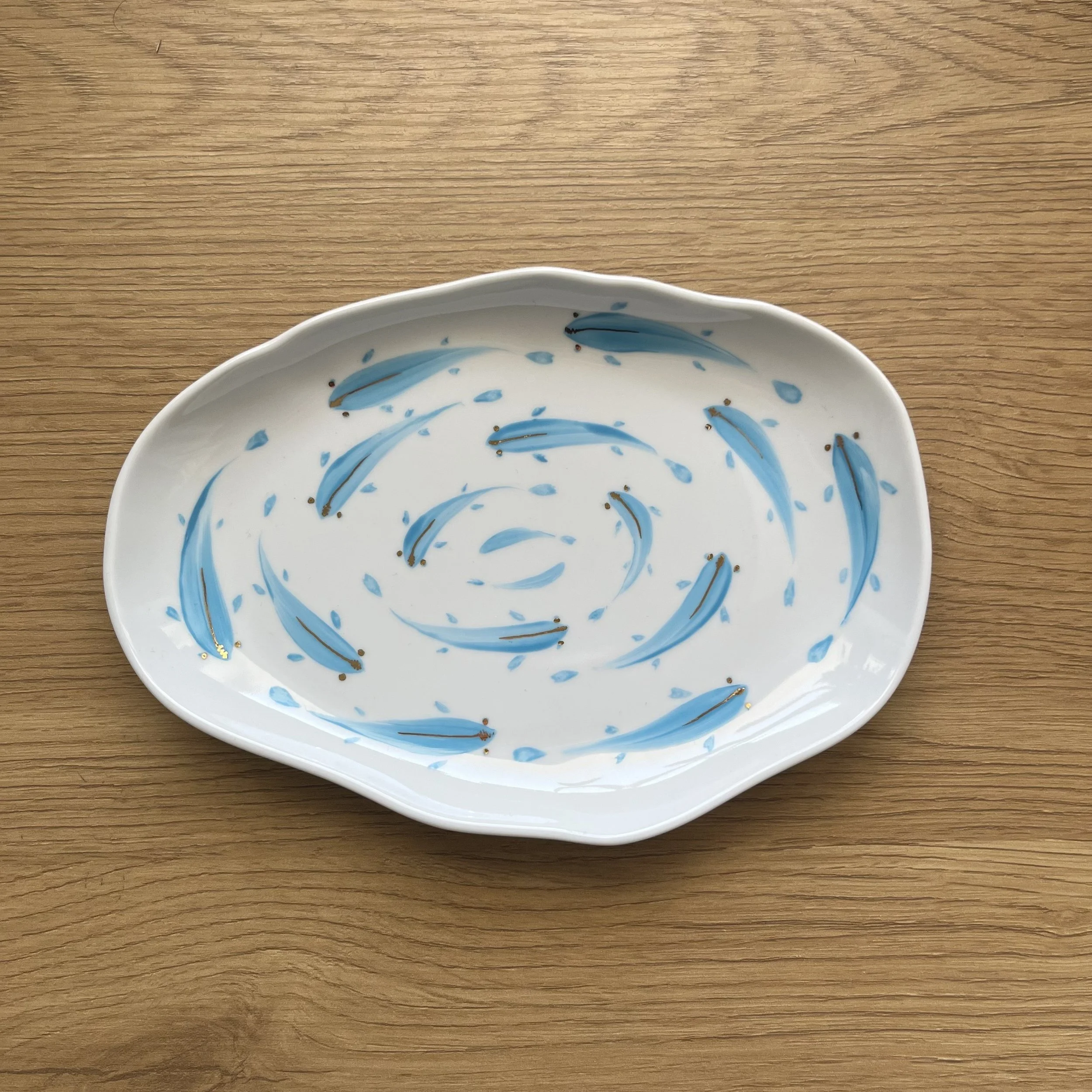 A white ceramic dish with a blue fish pattern on the inside, placed on a wooden surface.
