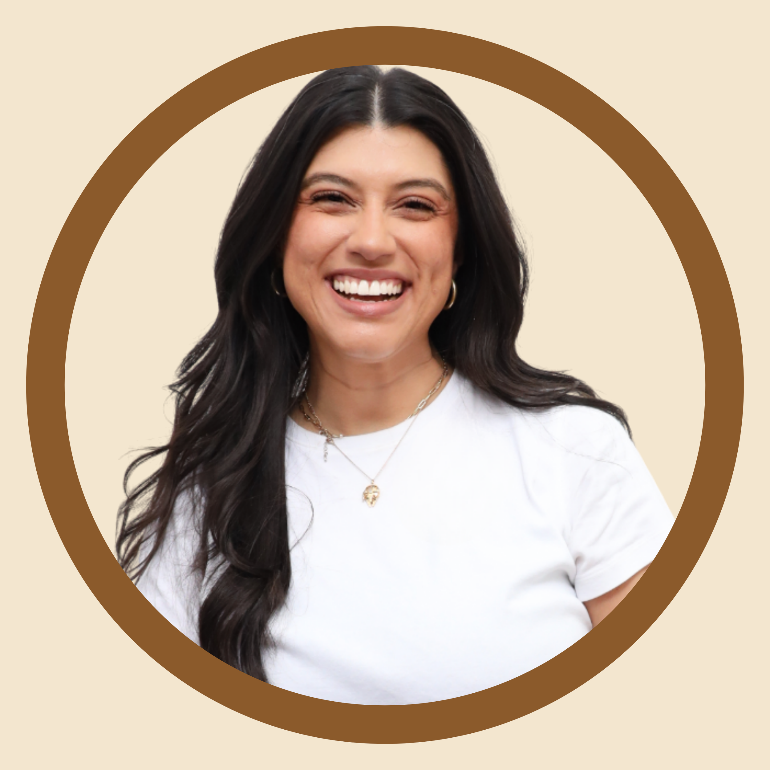 A woman with long dark hair, smiling widely, wearing a white shirt, gold jewelry, and hoops, in front of a beige background with a brown circular border.
