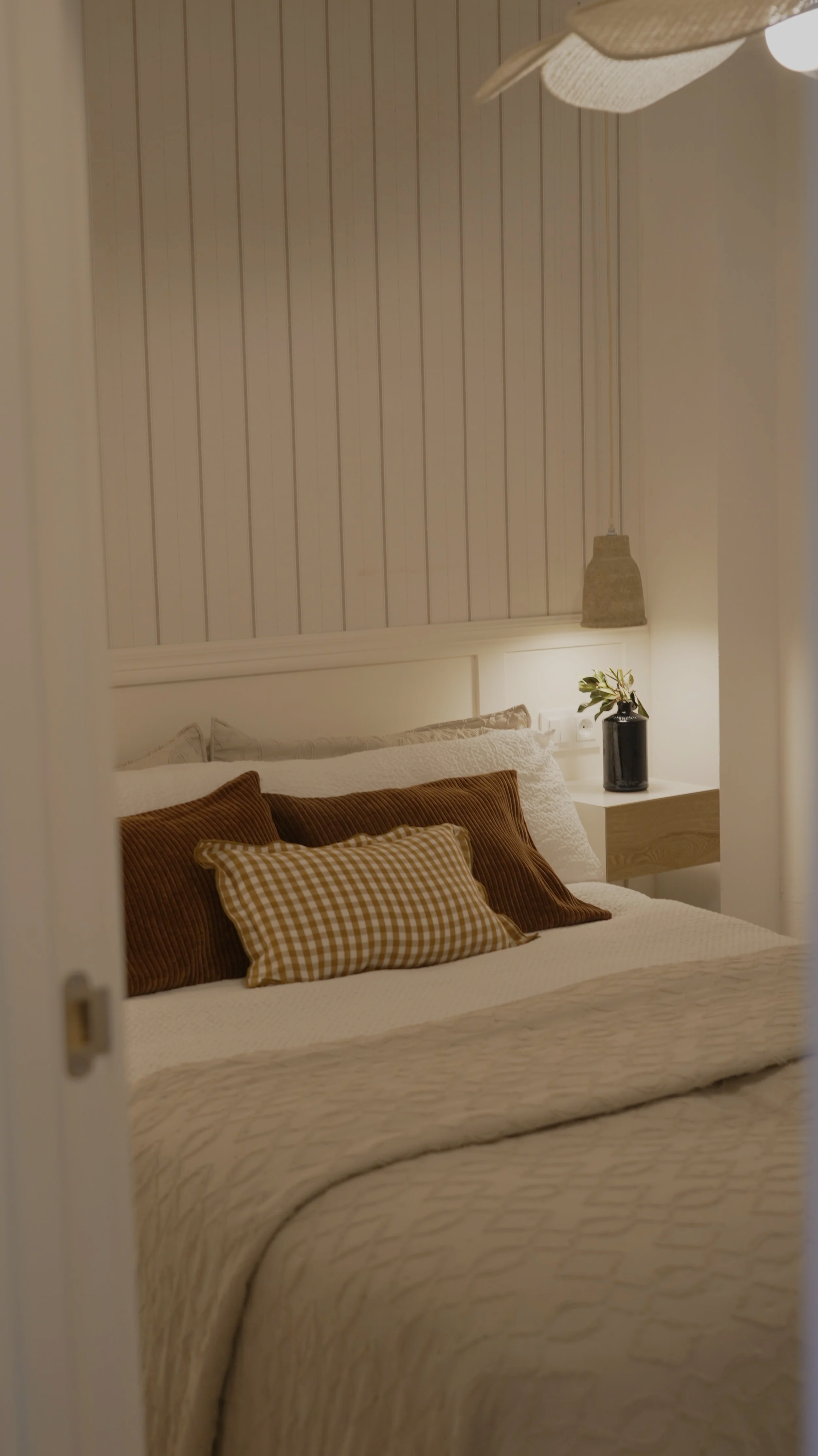 Cama con almohadas en habitación con paredes de madera y lámpara colgante.