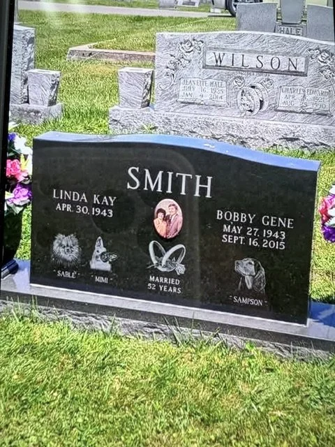 Gravestone with the surname 'Smith' and two names, Linda Kay and Bobby Gene, with their birth dates. The gravestone features a photo of the couple, symbols of a heart, a dog paw print, a dog head, and a dog with the name 'Sampson'.