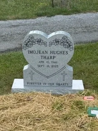 Gray granite gravestone with a heart shape, decorated with flowers, inscribed with the name Imojean Hughes, Tharp, born April 10, 1946, died September 18, 2025, and the phrase Forever in Our Hearts, two crosses, and placed on a grassy area.