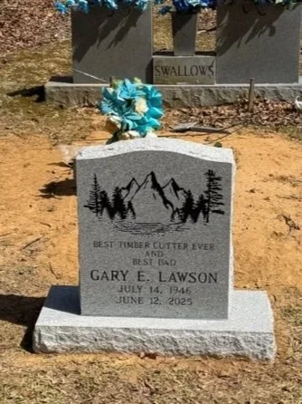 Gravestone with mountains, trees, and a blue floral decoration.