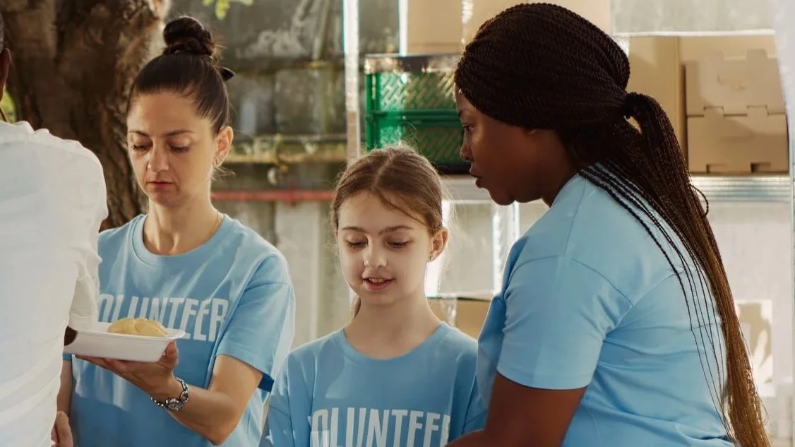Three women and a girl wearing blue volunteer t-shirts working together, preparing or serving food.