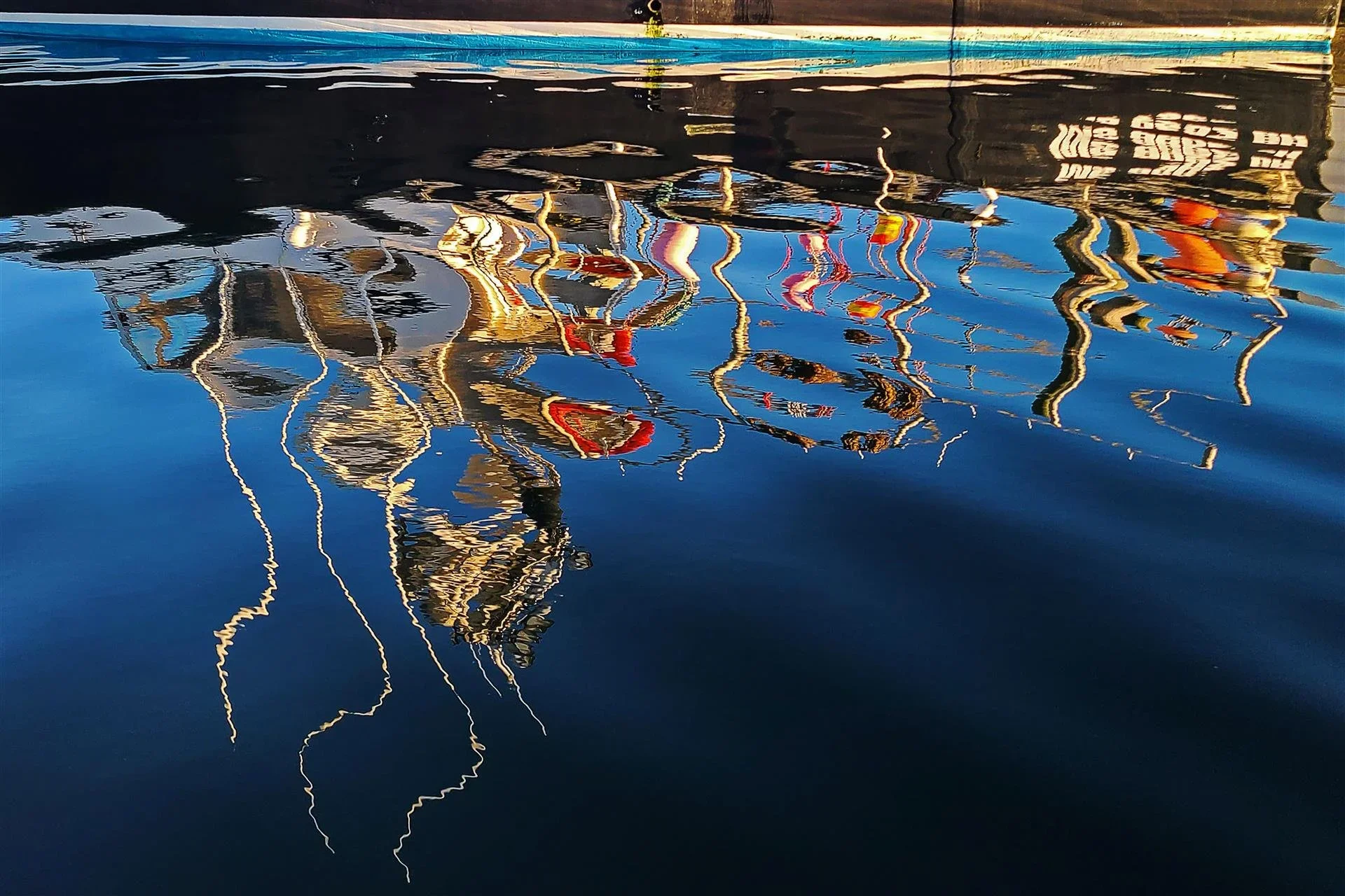 Reflection of boats and their masts on water in a harbor or marina.