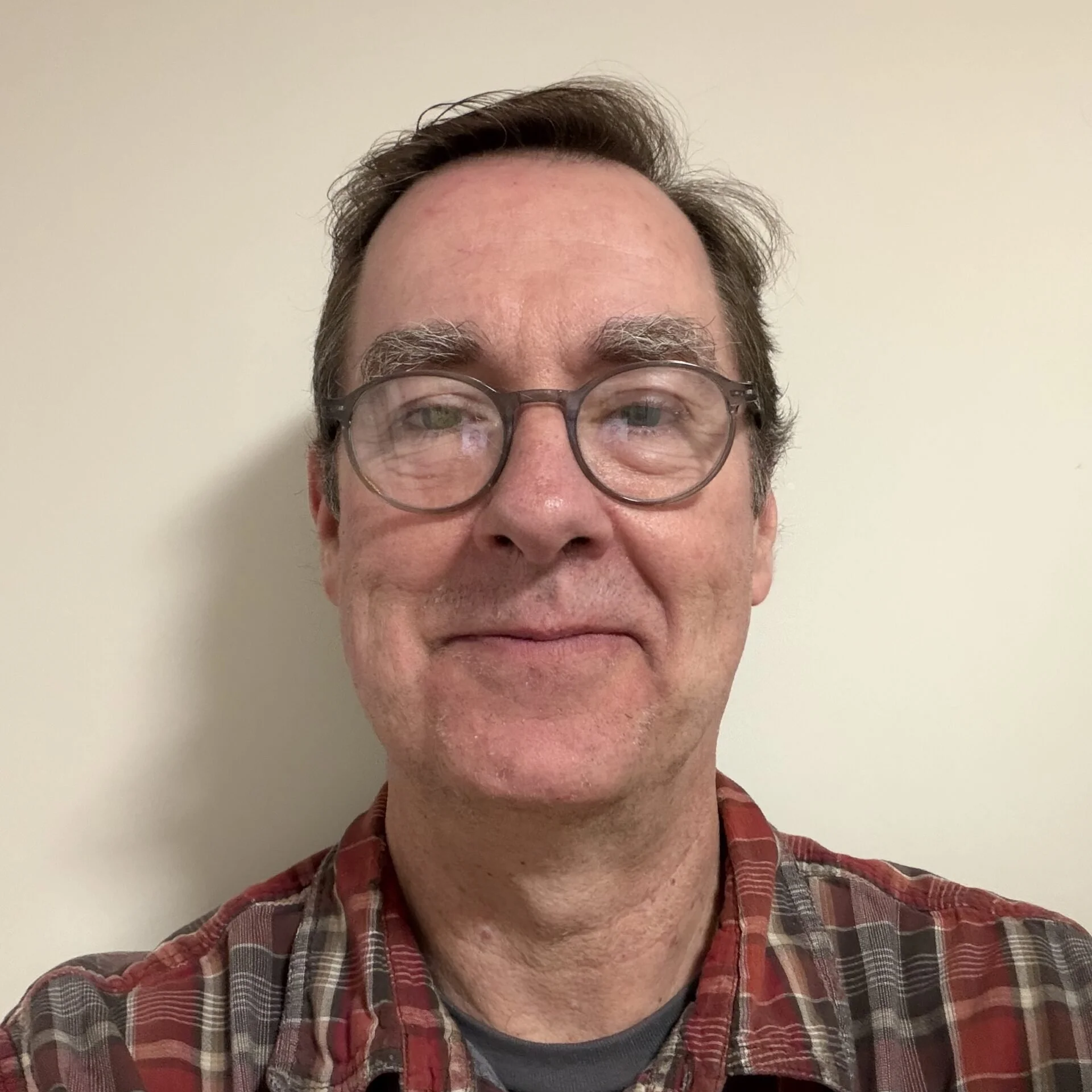 Close-up of a middle-aged man with glasses smiling against a plain light-colored wall.