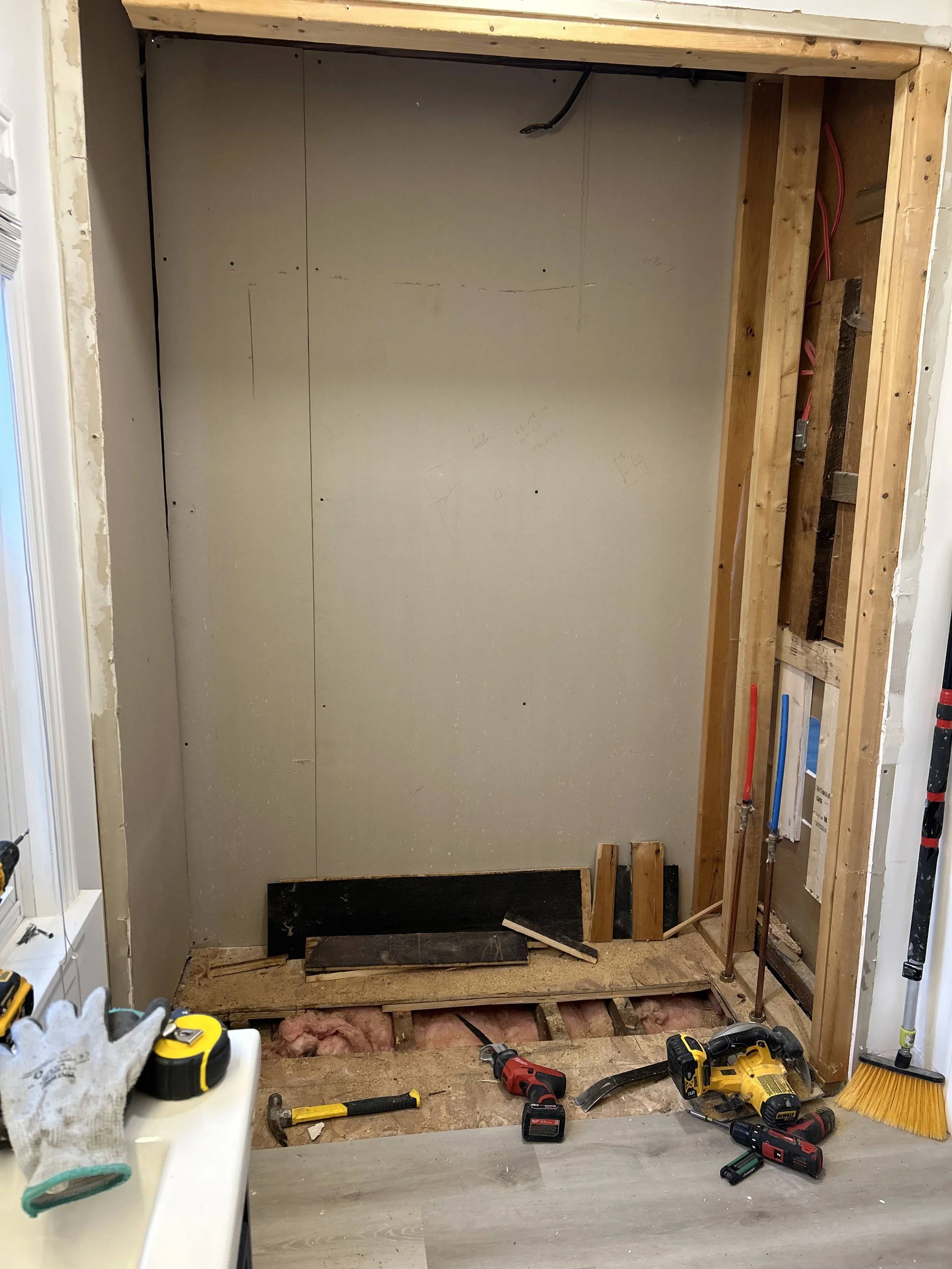 Interior view of a bathroom under renovation with drywall installation and construction tools on the floor, including a hammer, cordless drill, and cordless impact driver.