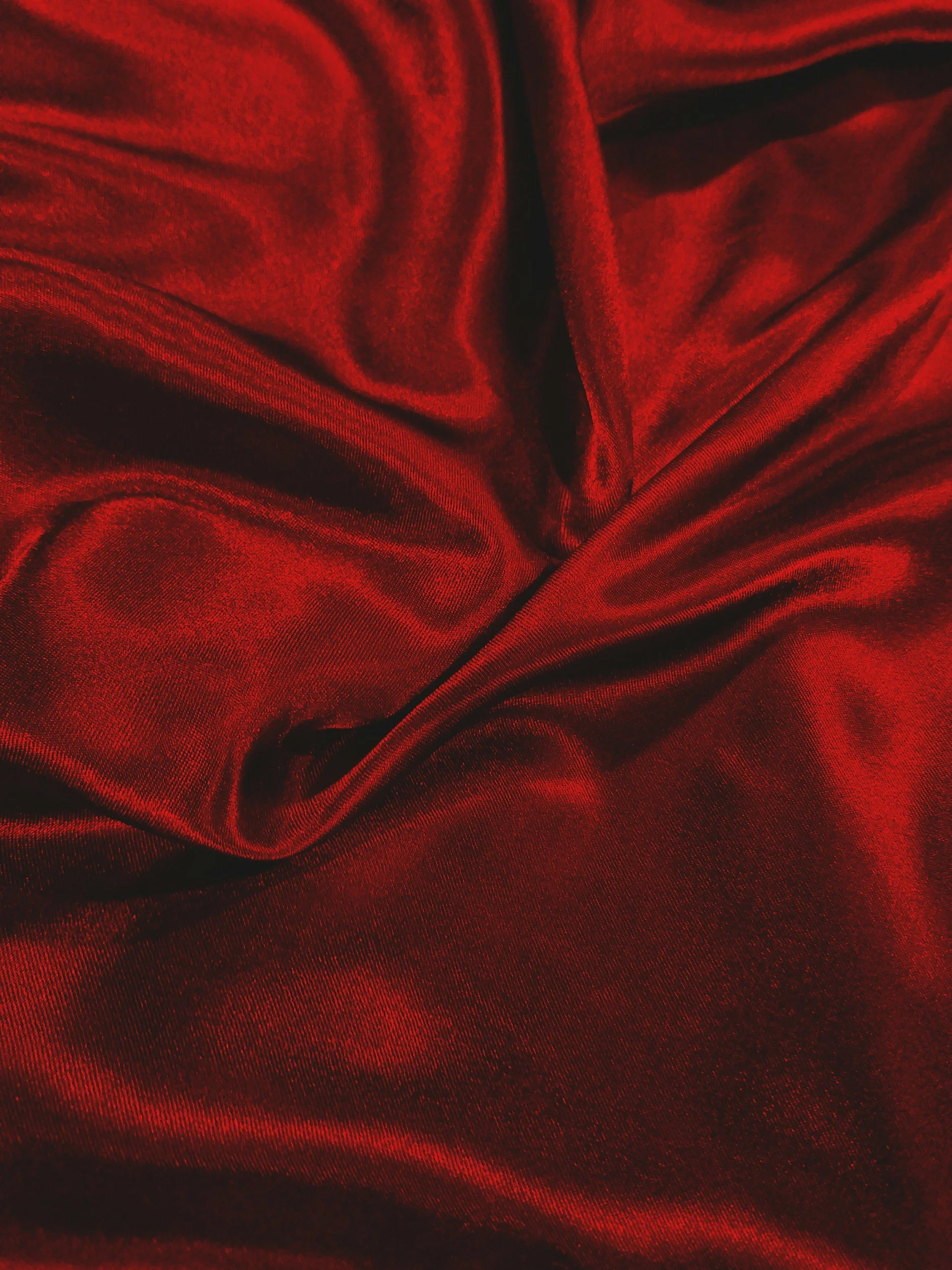 Close-up of shiny red satin fabric with folds and creases.
